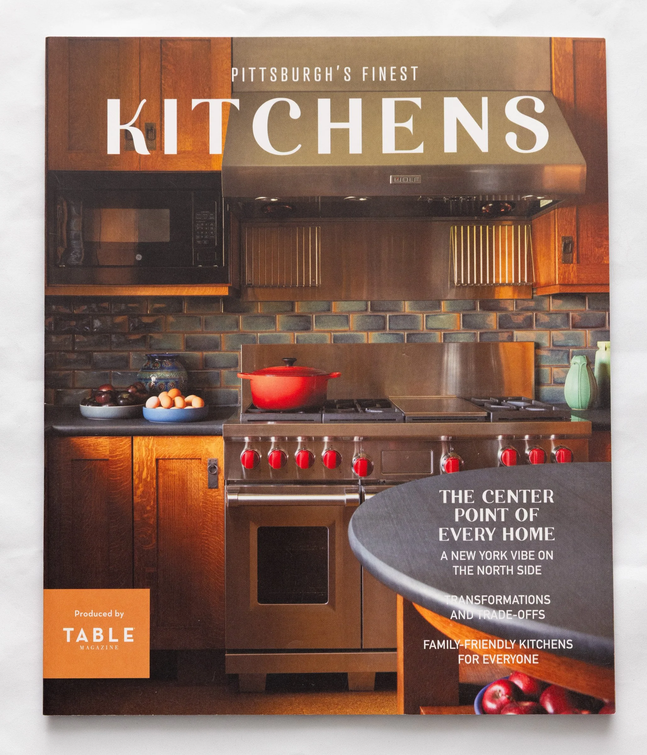 Magazine cover titled "Pittsburgh's Finest Kitchens" featuring a kitchen with wood cabinets, a stainless steel stove, a red pot, a microwave, and a brick backsplash.