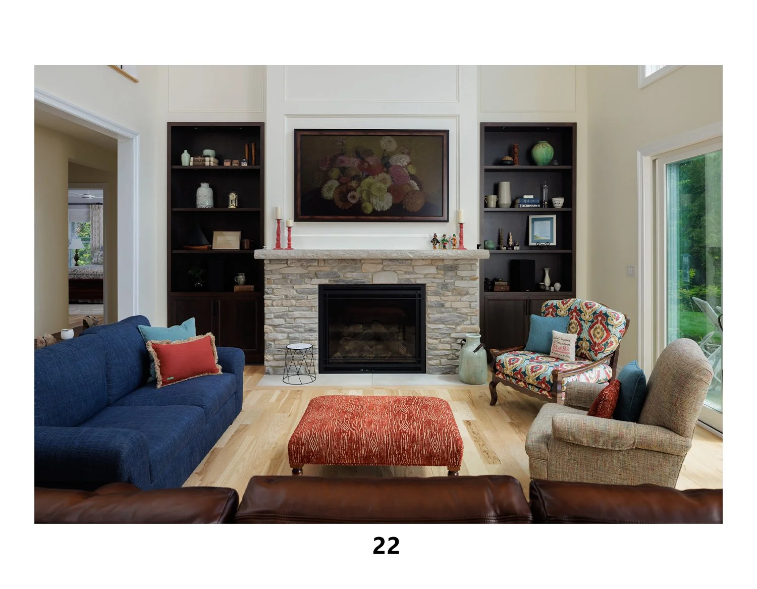 Living room with fireplace, blue sofa, colorful armchair, red ottoman, and built-in shelves.