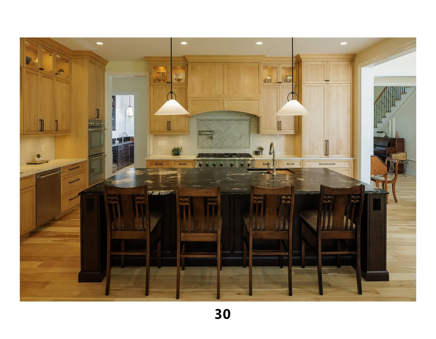 Kitchen with light wood cabinets, a black marble island, pendant lighting, and a stainless steel stove, with a doorway to a dining or living area on the right.