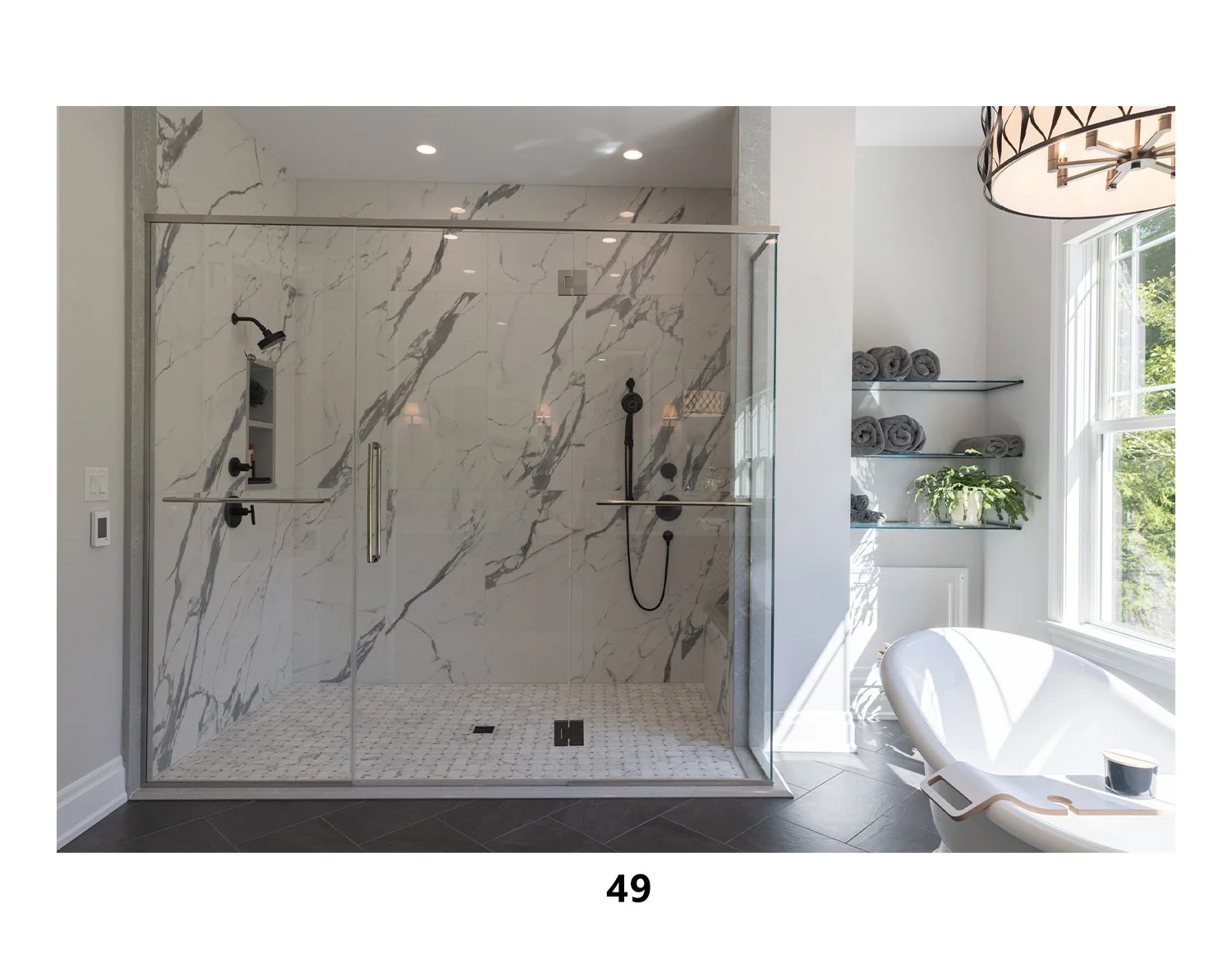 Modern bathroom with glass-enclosed shower with marble walls, built-in shower niches, and black fixtures. To the right, a large window lets in natural light, revealing gray rolled towels on glass shelves and a potted plant. A white bathtub with a dig
