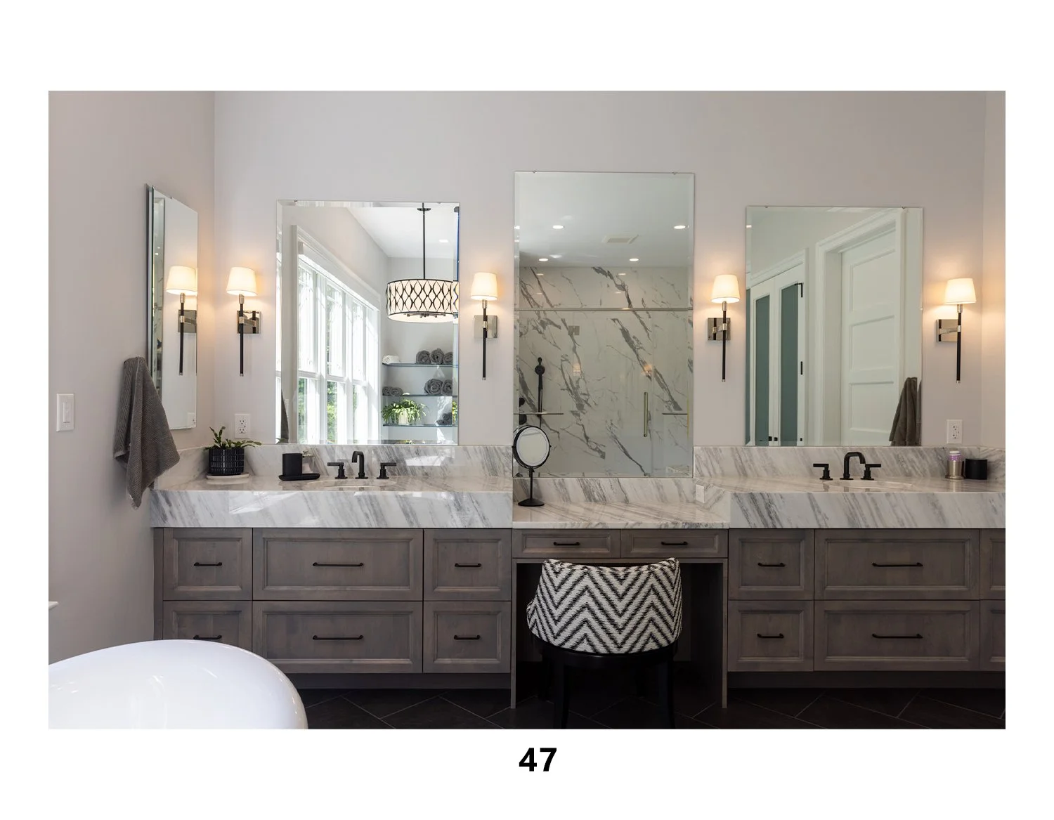 Modern bathroom vanity with double sinks, marble countertops, dark wood cabinets, large mirrors, wall-mounted lamps, and a glass-enclosed shower with marble walls.