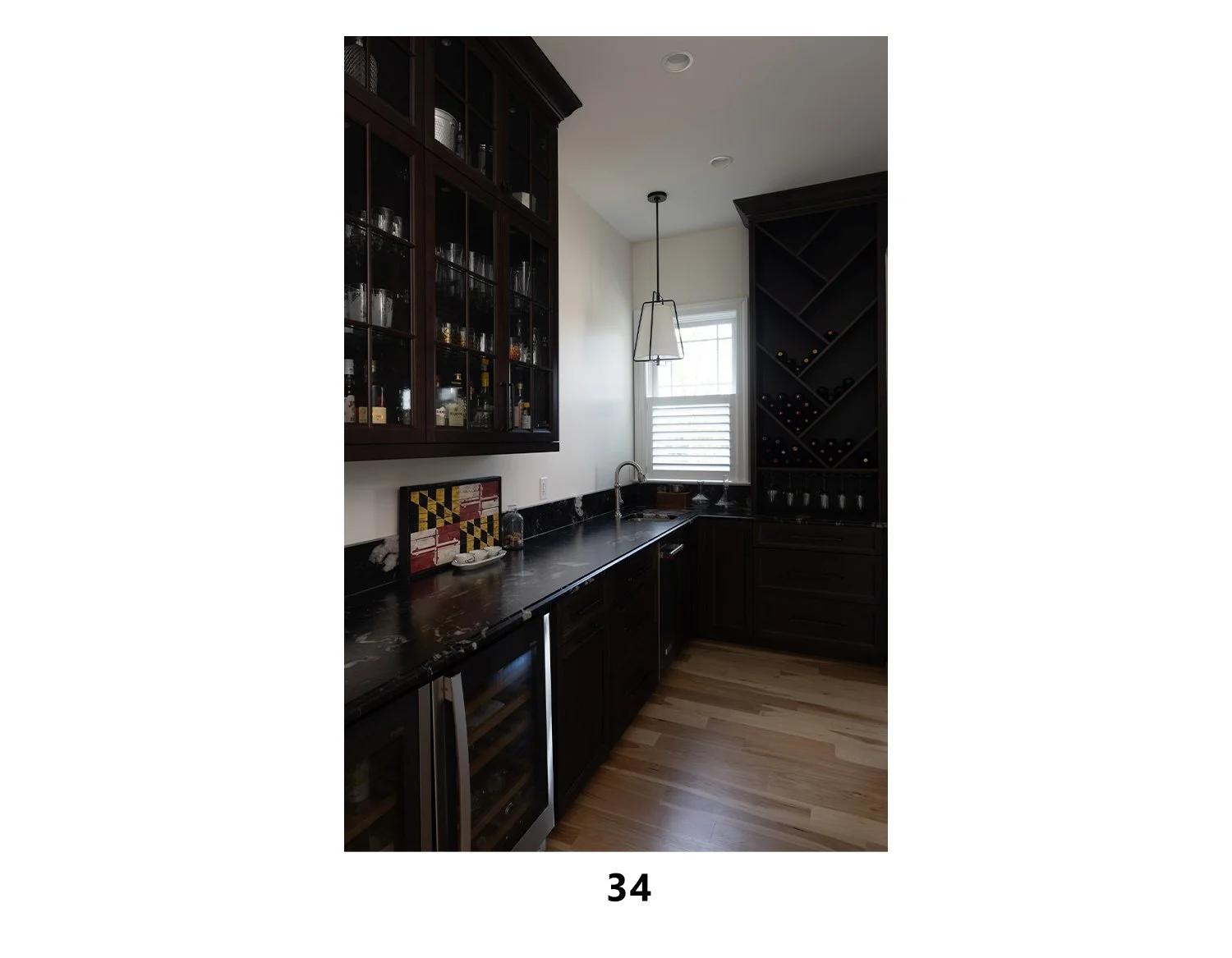 Contemporary kitchen with dark wood cabinets, black marble countertop, wine storage, a window with blinds, a white-paneled wall, and a hanging light fixture.