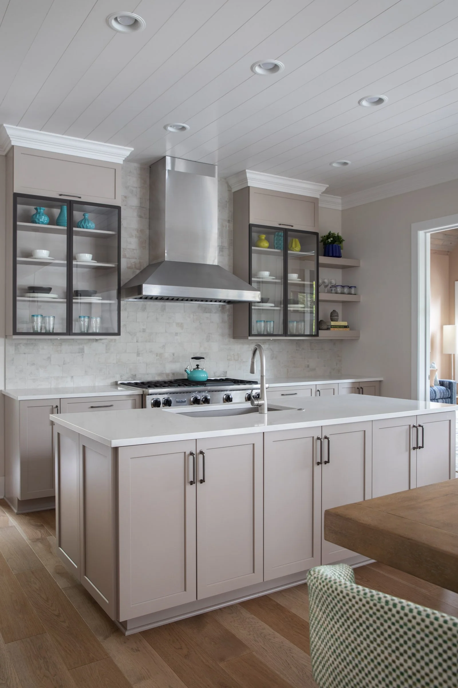 Modern kitchen with beige cabinets, open glass-fronted cabinets, a stainless steel range hood, and a wooden dining table.