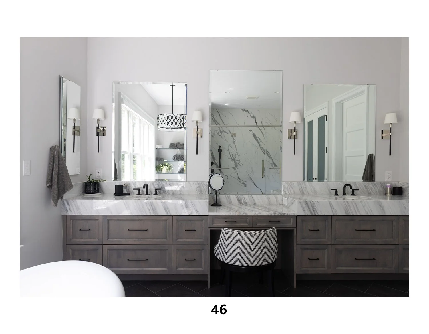 Modern bathroom with dual vanity sinks, marble countertops, gray wood cabinets, large mirrors, wall sconces, and a glass-enclosed shower with marble walls.