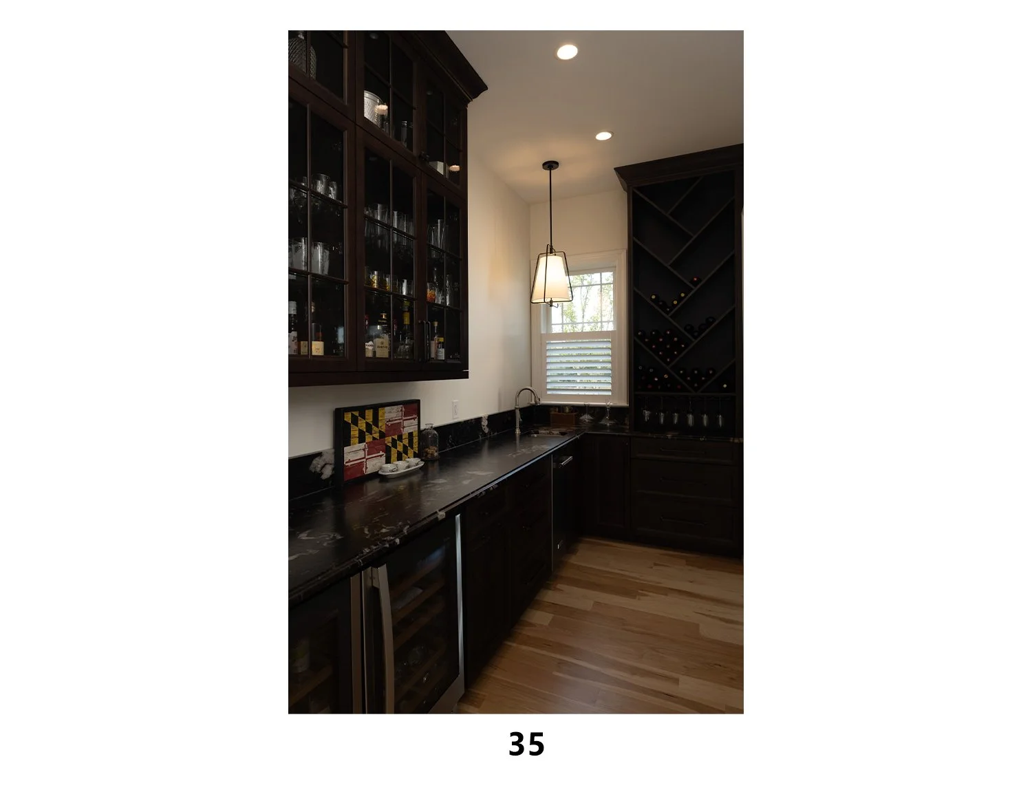 Dark wood kitchen with upper and lower cabinets, wine rack, marble countertops, small wine cooler, window with blinds, and pendant lighting.