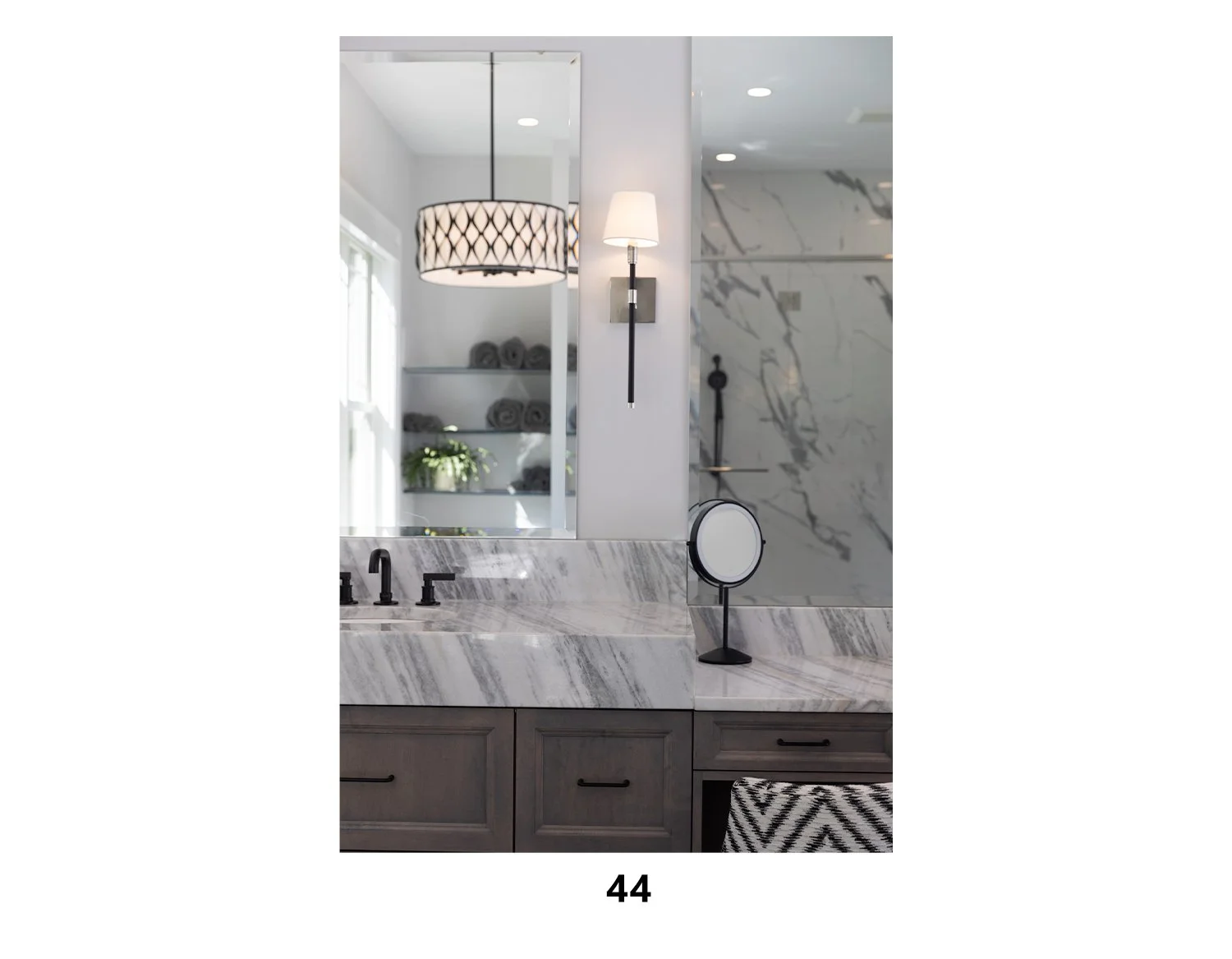 A modern bathroom with a marble countertop, a mirror, a wall-mounted light fixture, a small mirror on a stand, and shelves with towels and plants.