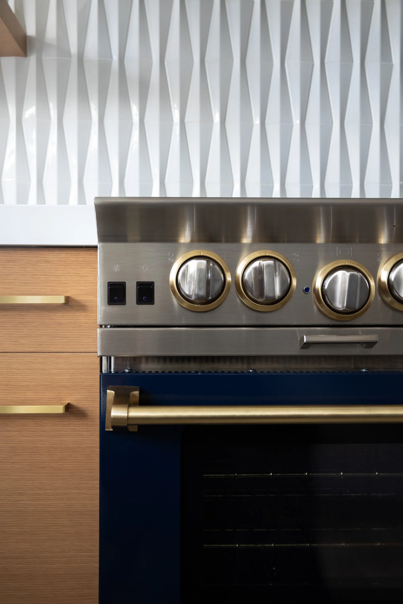 Close-up of a modern kitchen stove and oven with a white geometric backsplash and wooden cabinetry. Interior design photography
