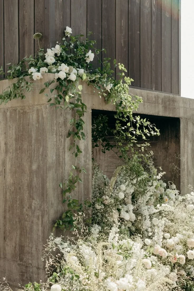 A concrete fireplace with floral arrangements, including white roses and greenery, cascading over the top and down the sides.