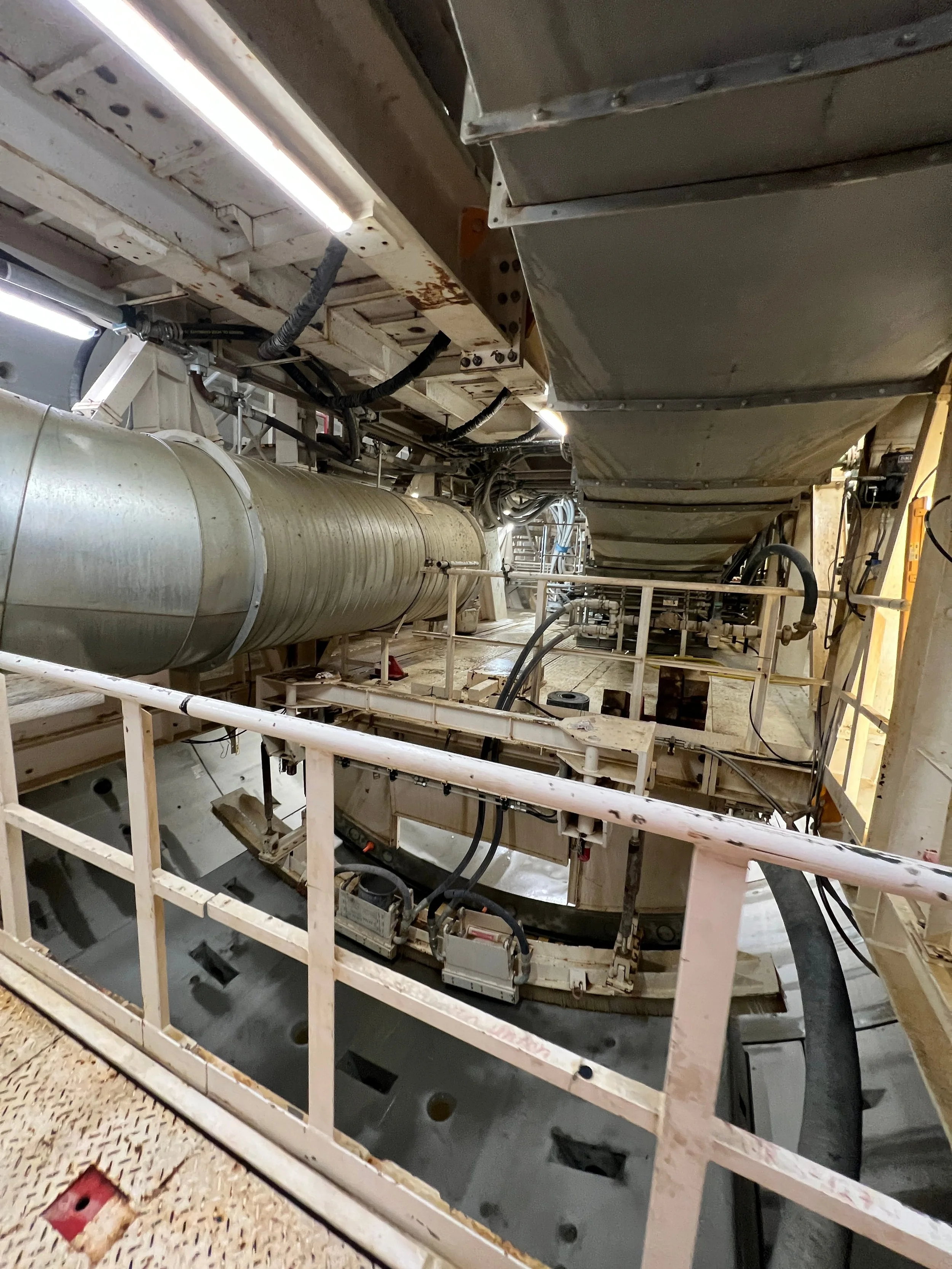 Industrial or spaceship interior with large metallic tube, grating floor, and various pipes and cables.
