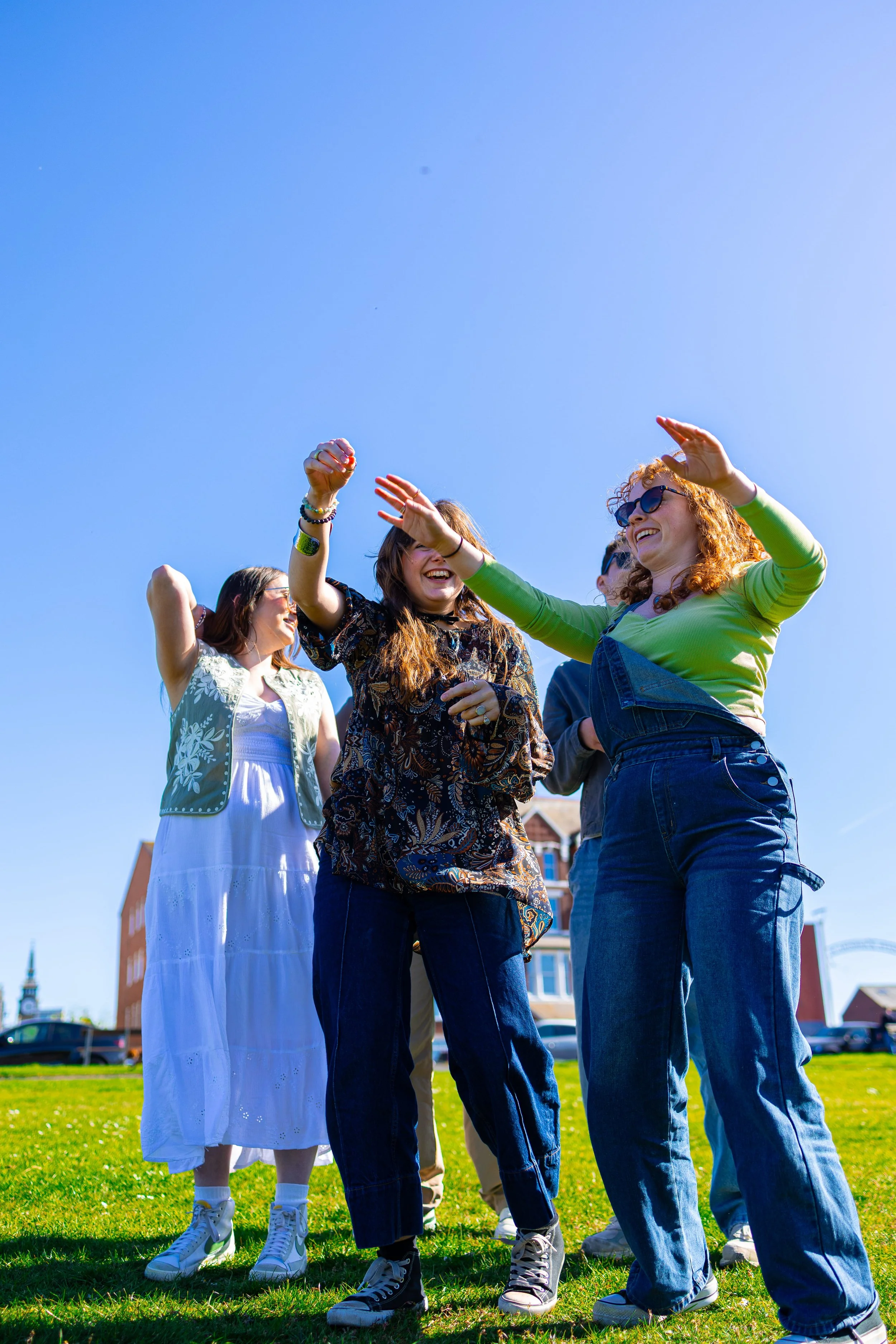A group of cheerful young women and a girl enjoying outdoor activities on a sunny day at a park, wearing casual clothing and sunglasses.