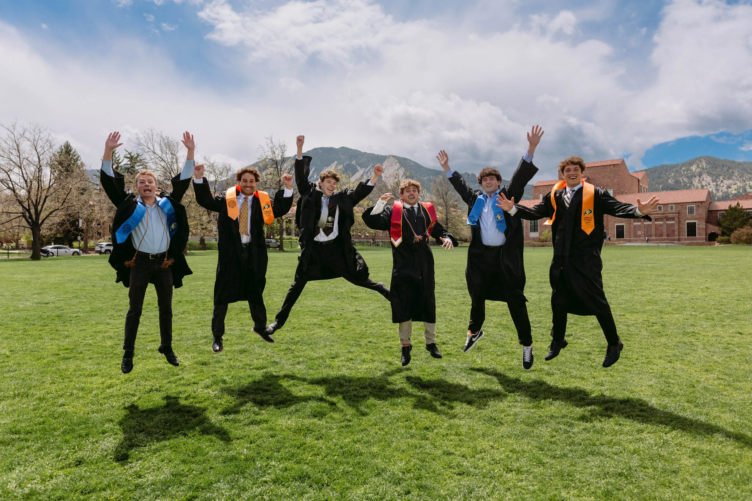 Group graduation photo of six CU Boulder seniors jumping in front of the Flatirons at Chautauqua Park, capturing fun energy, candid action, and Boulder scenery.