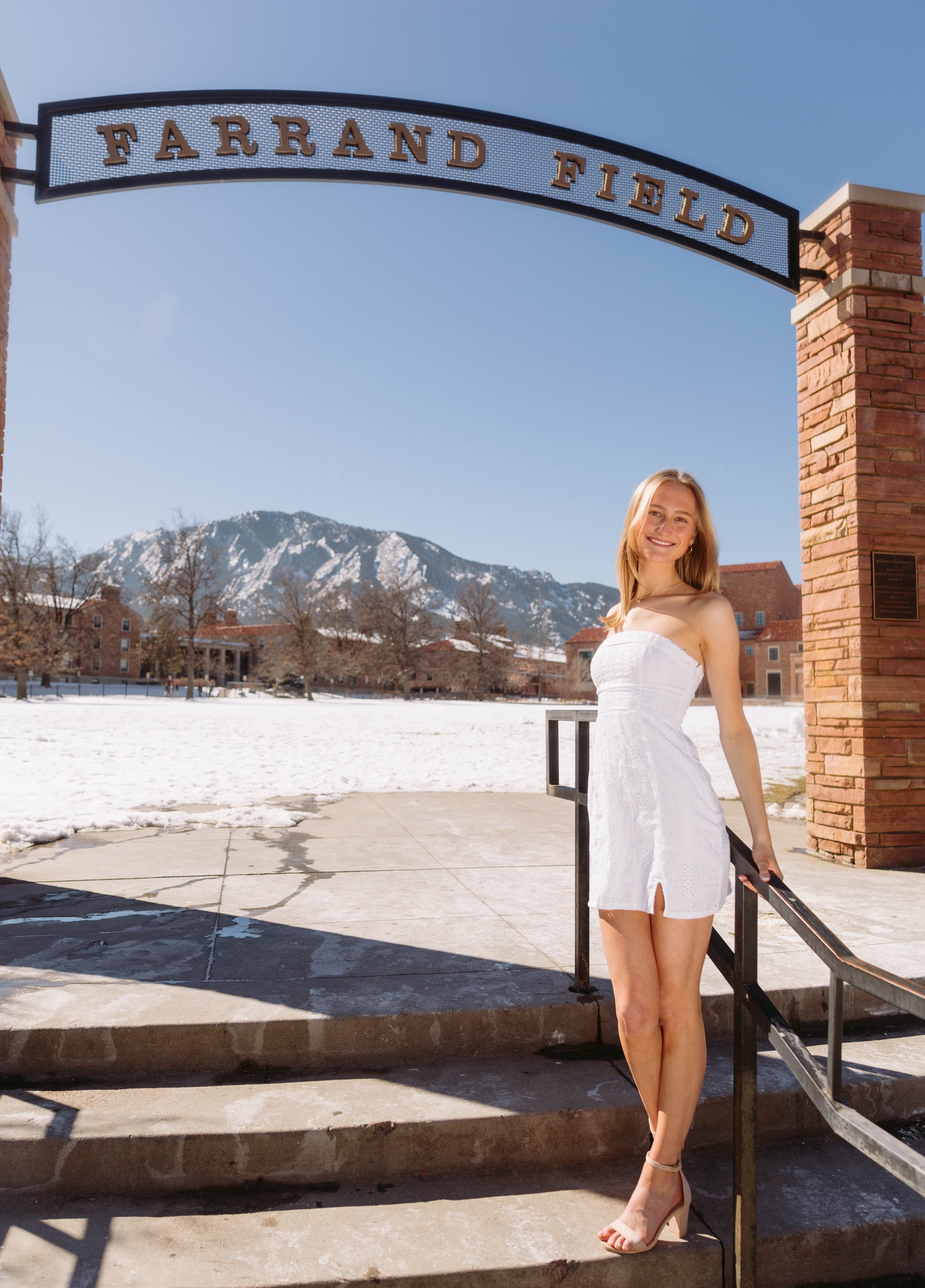CU Boulder senior portrait of a graduate standing on campus steps with snow and the Flatirons in the background, featuring clean, bright natural light.