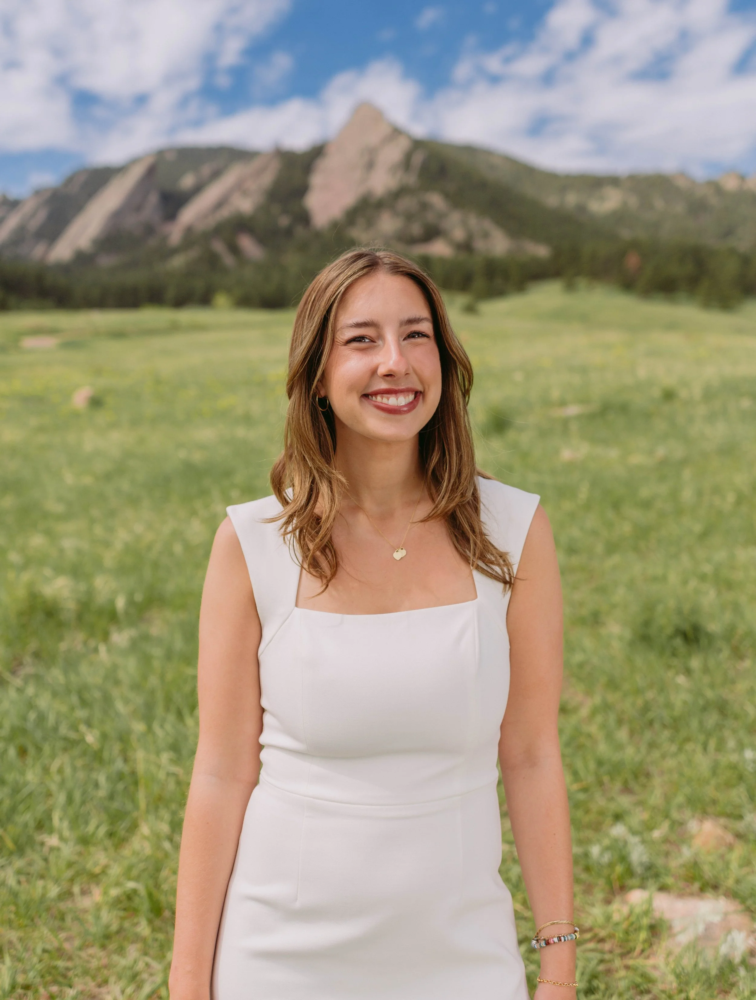 CU Boulder senior portrait smiling in green field with Flatirons mountains
