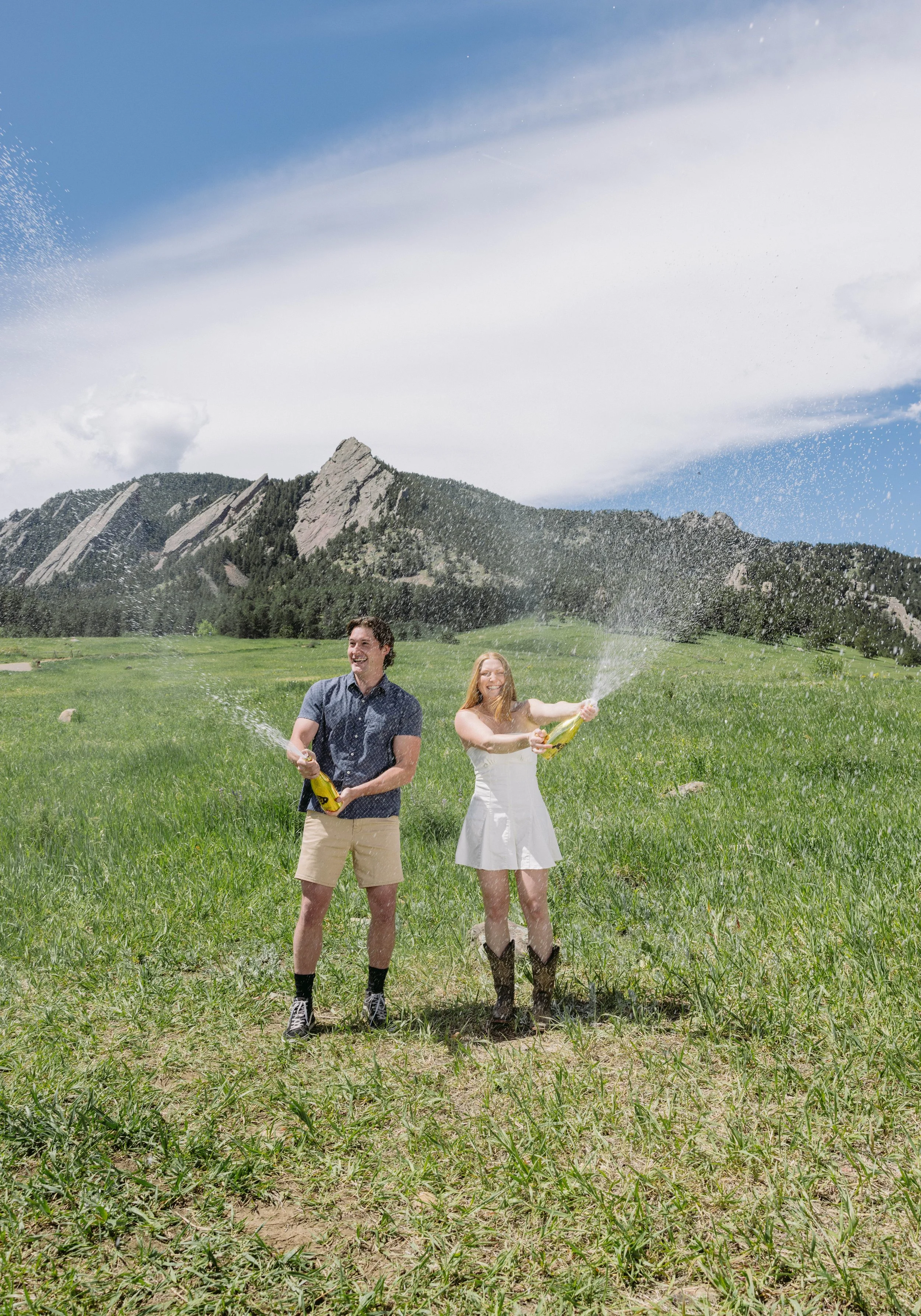 CU Boulder seniors celebrating graduation with champagne spray in field near Flatirons