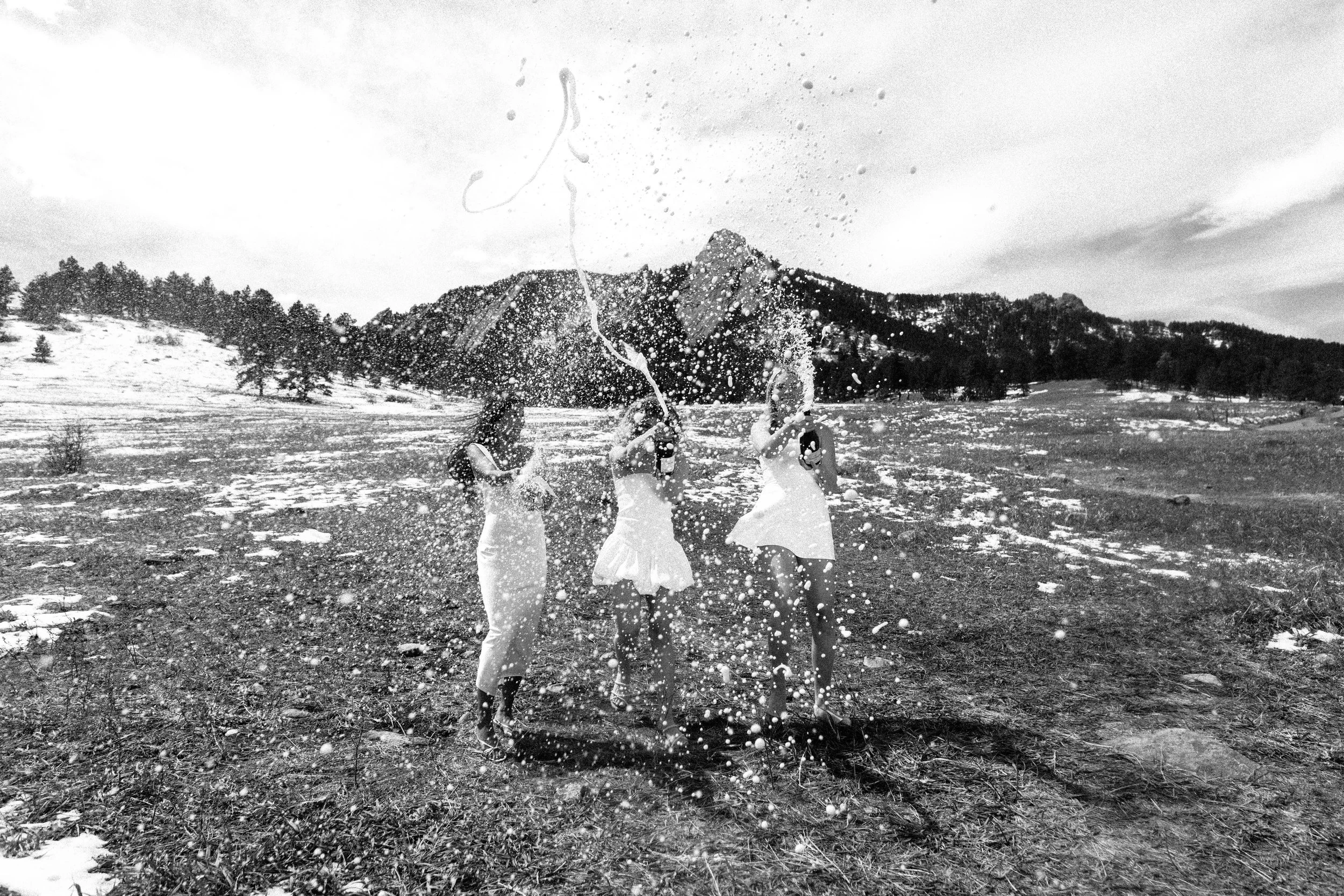 CU Boulder seniors celebrating graduation with champagne spray in snowy field with Flatirons