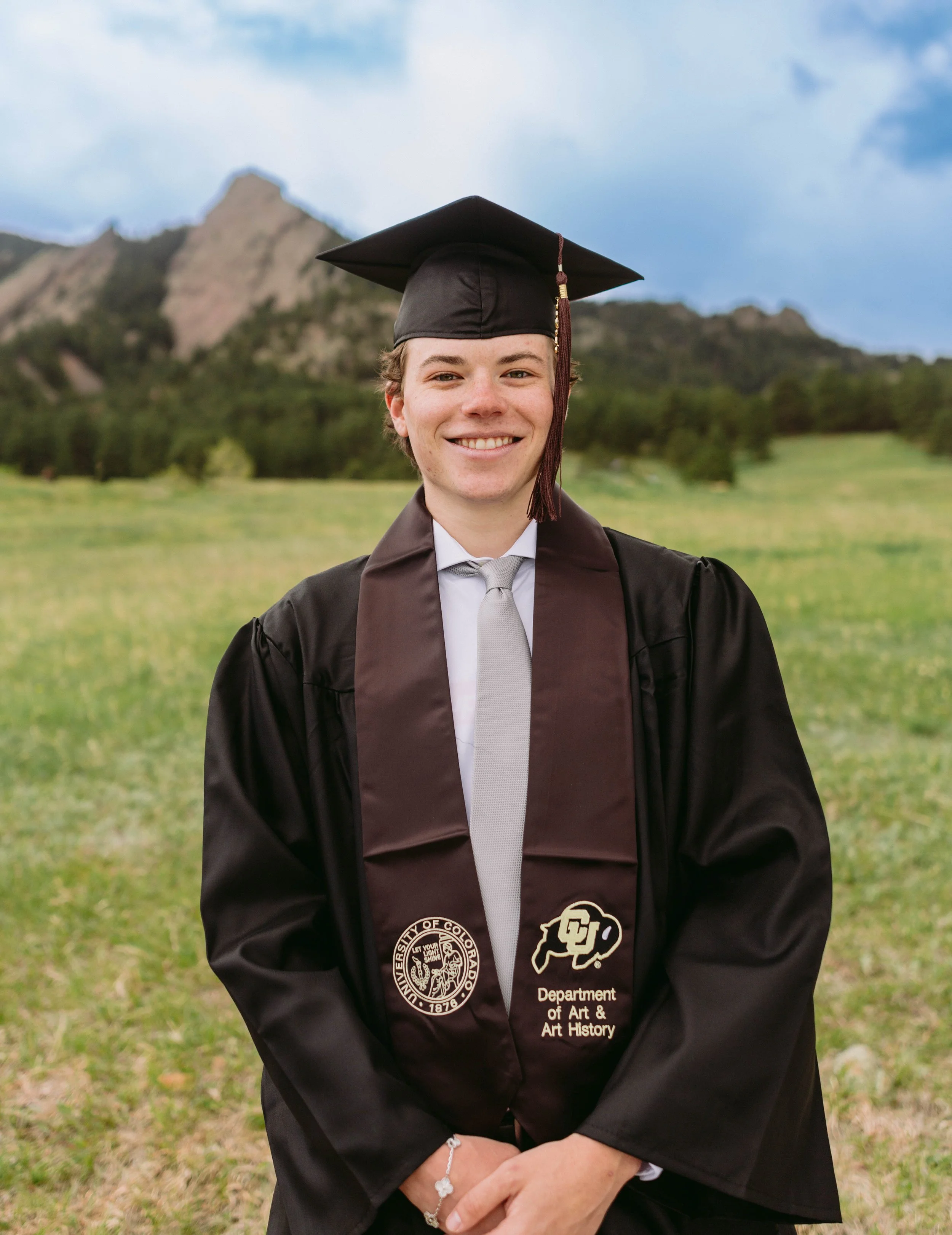 CU Boulder senior portrait in cap and gown at Chautauqua Park with Flatirons backdrop
