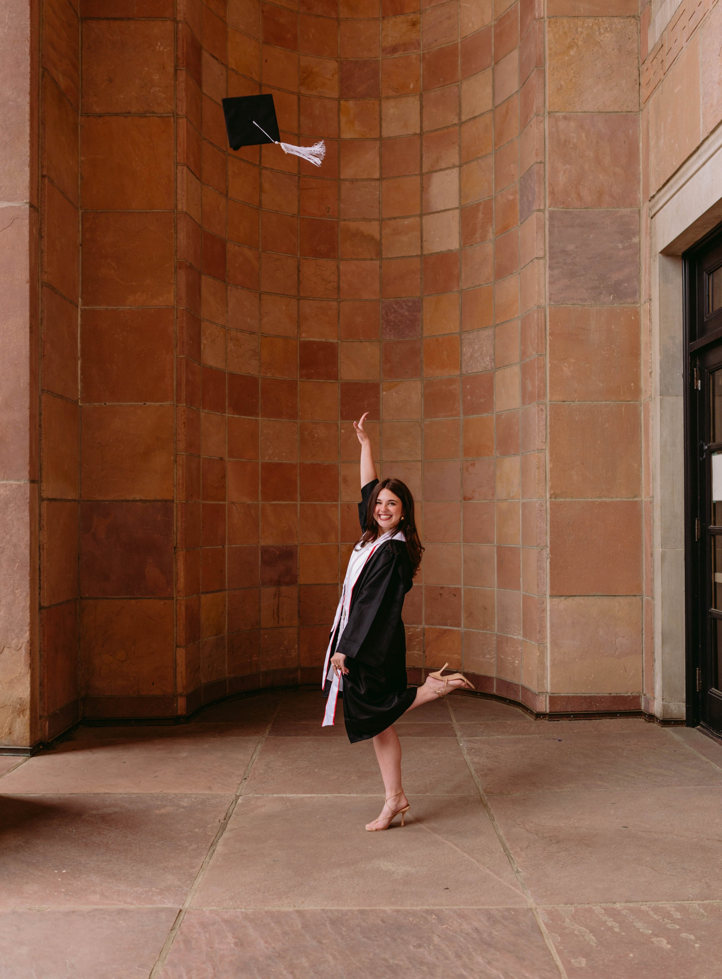 CU Boulder senior celebrating graduation under campus archway wearing cap and gown