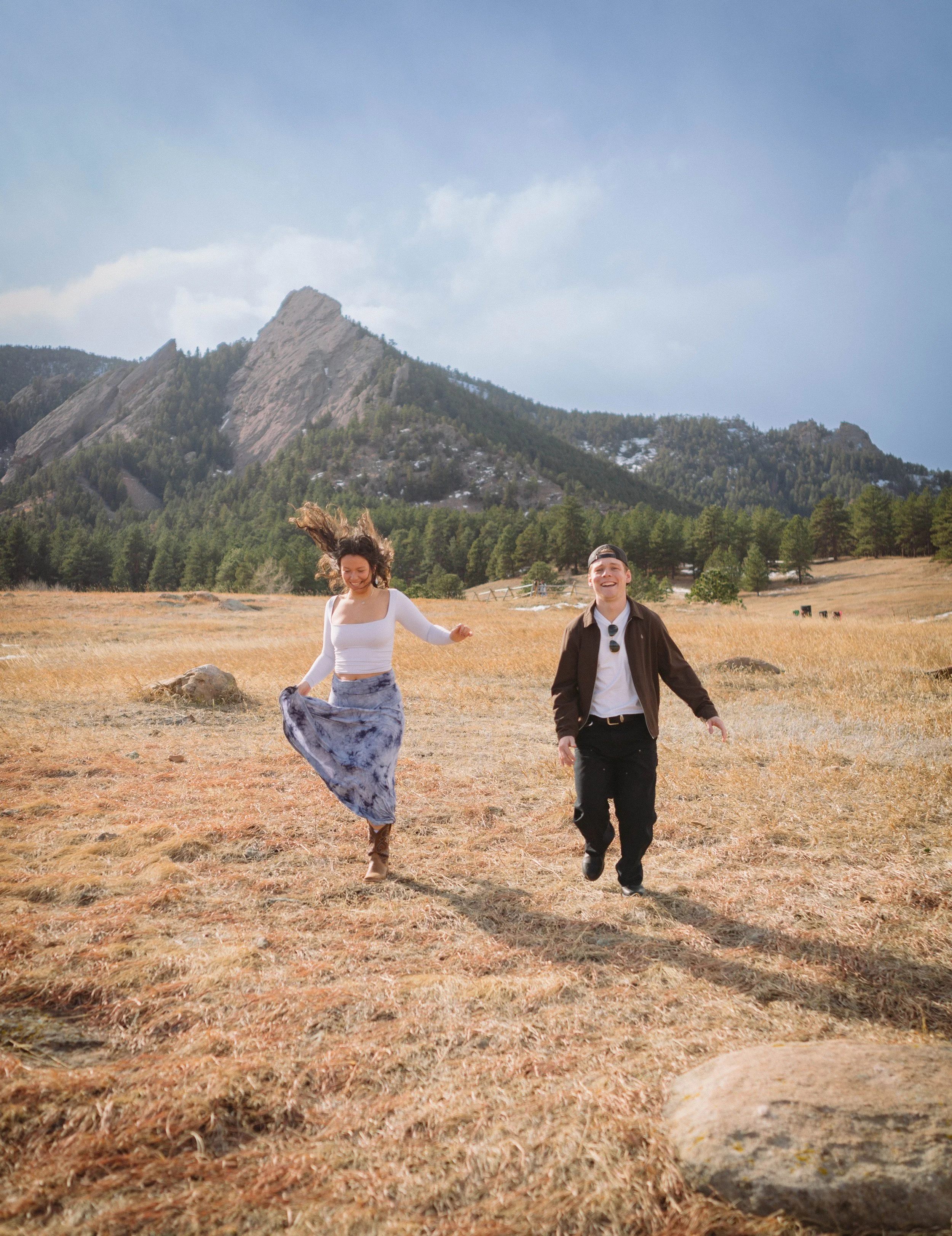CU Boulder senior couple celebrating graduation in open field with Flatirons mountains