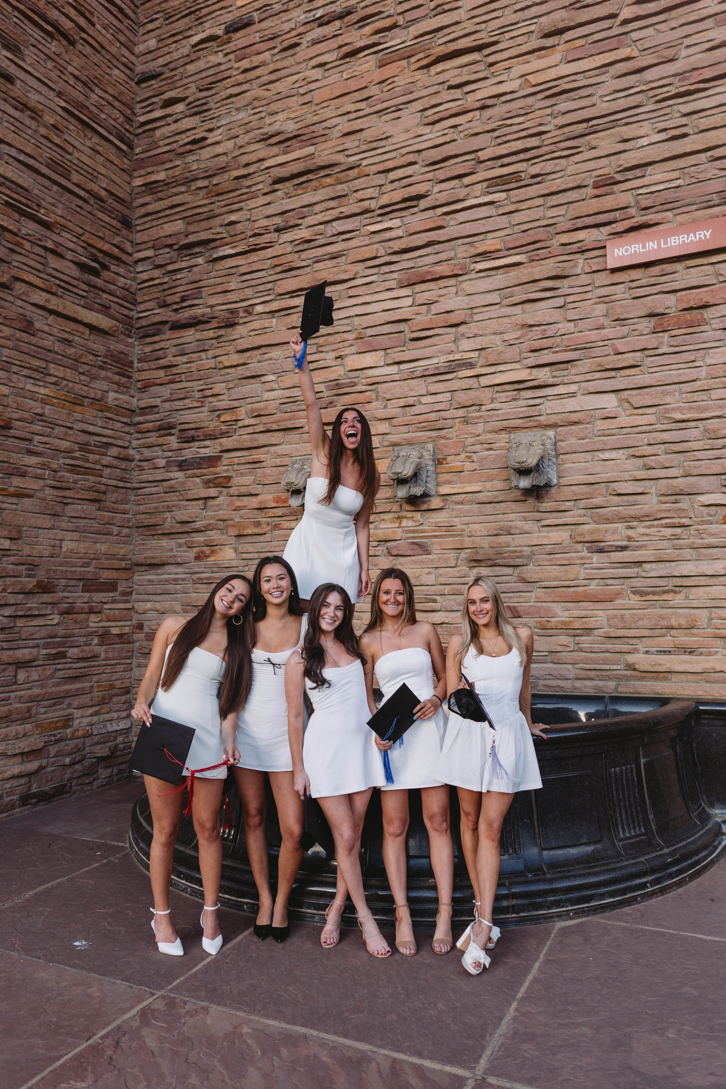 Group of CU Boulder seniors celebrating graduation in white dresses outside Norlin Library