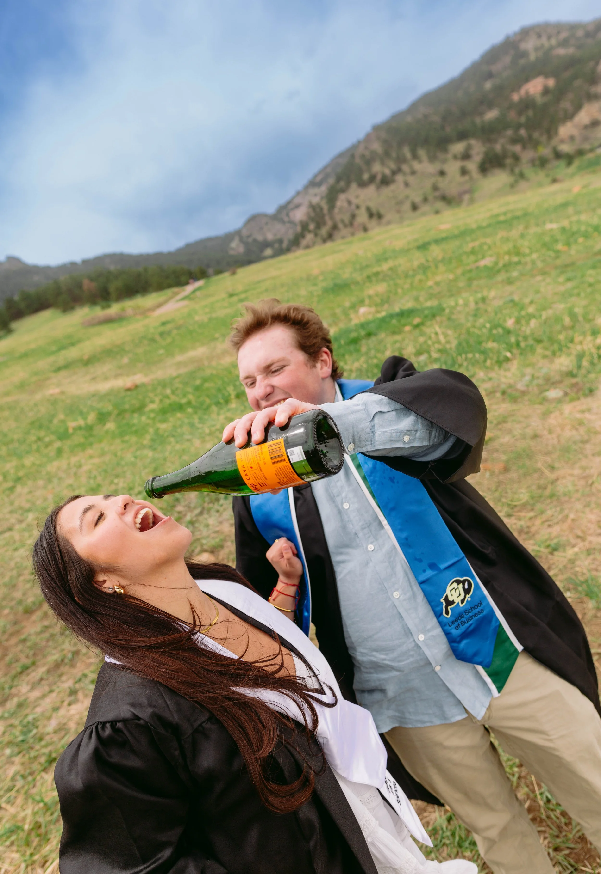 CU Boulder senior portrait wearing graduation stole in grassy field with Flatirons mountains
