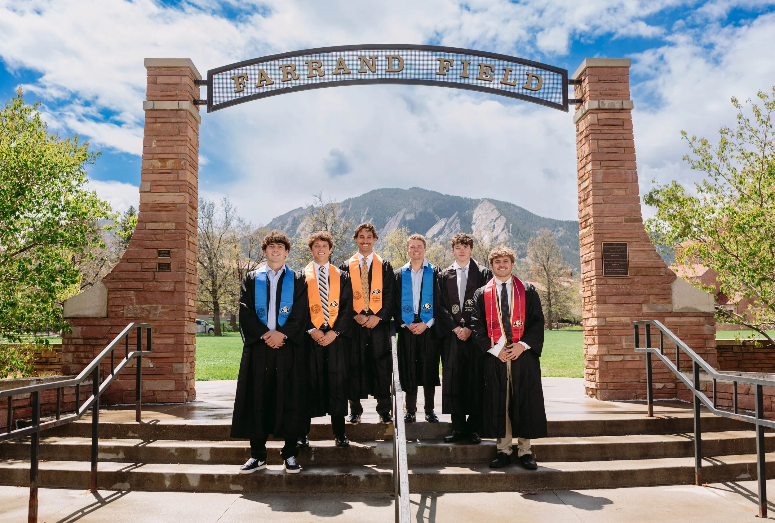 Group of CU Boulder male graduates posing together at Farrand Field in caps and gowns