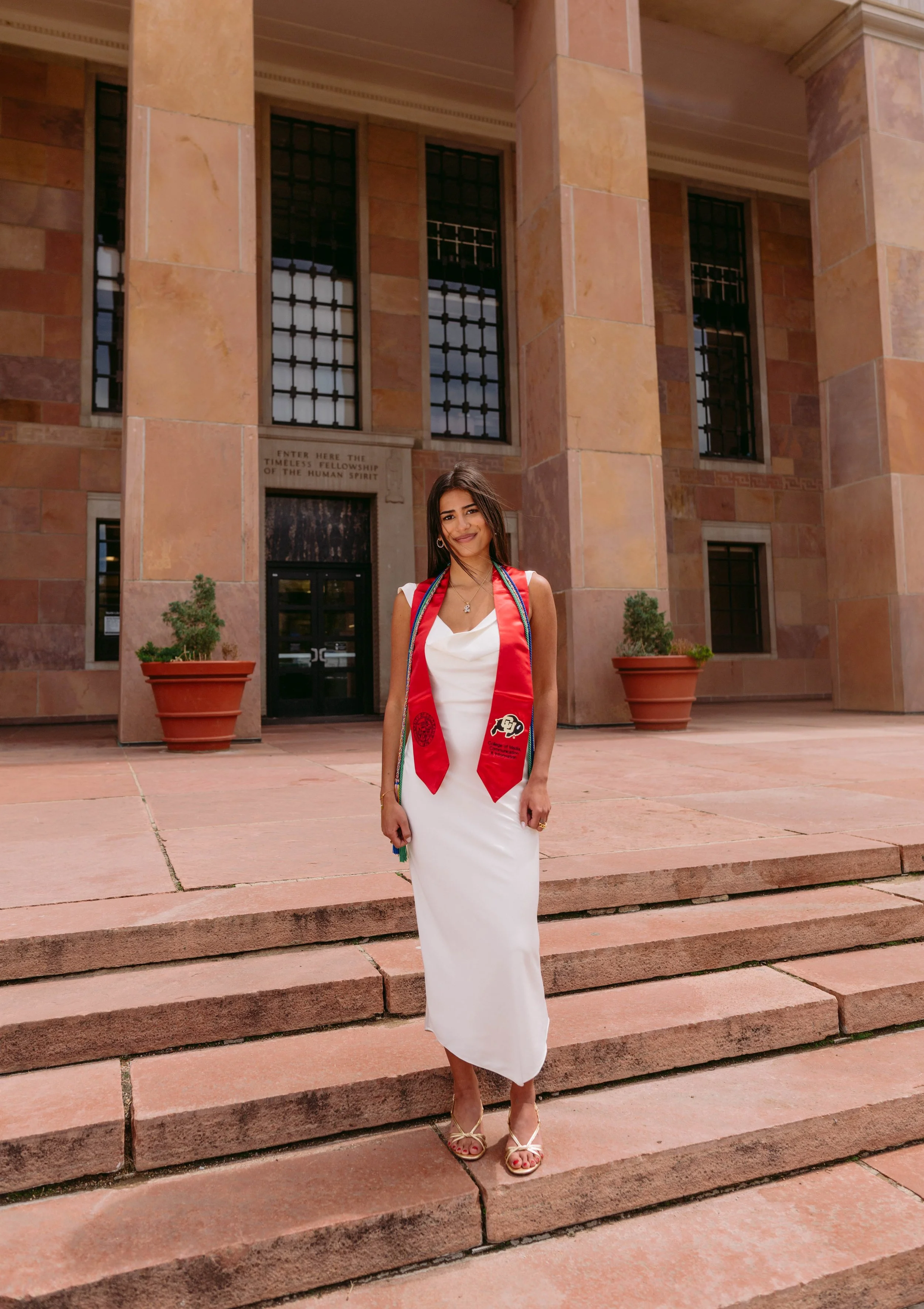 CU Boulder senior portrait on campus steps wearing graduation stole and white dress