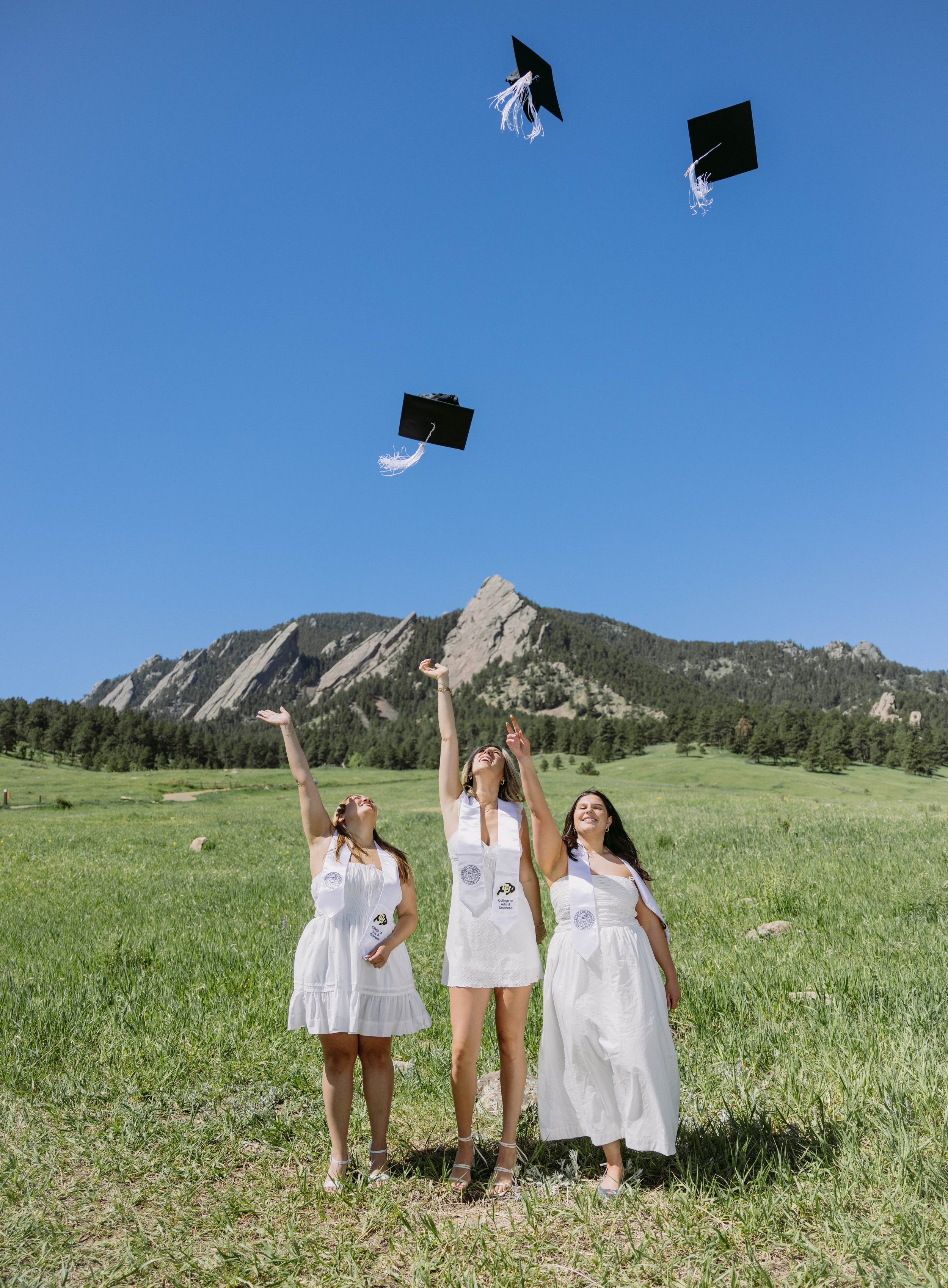 CU Boulder seniors tossing graduation caps at Chautauqua Park with Flatirons backdrop