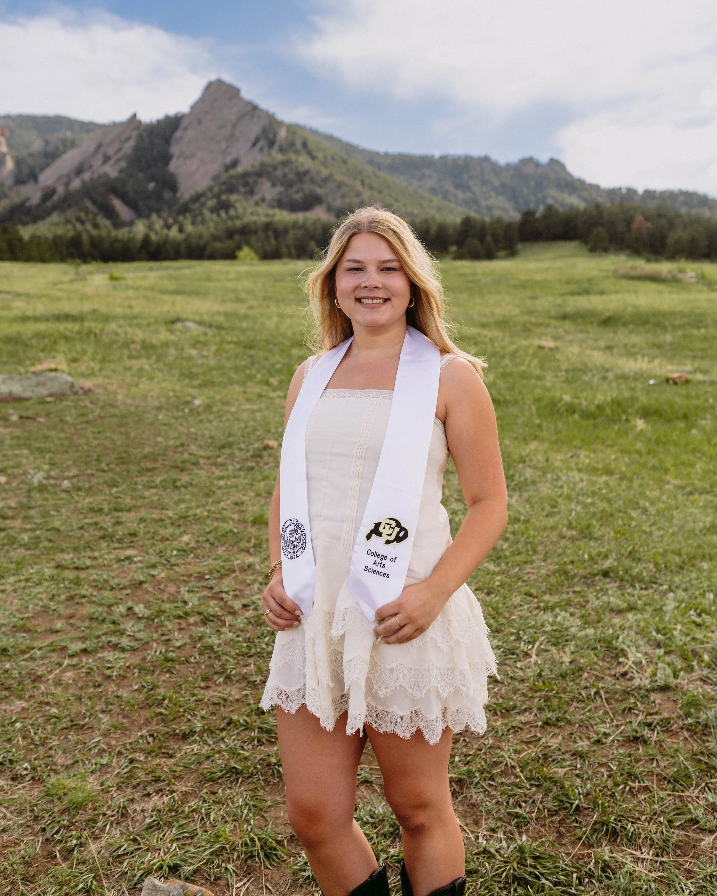 CU Boulder senior portrait in white dress with graduation stole and Flatirons backdrop
