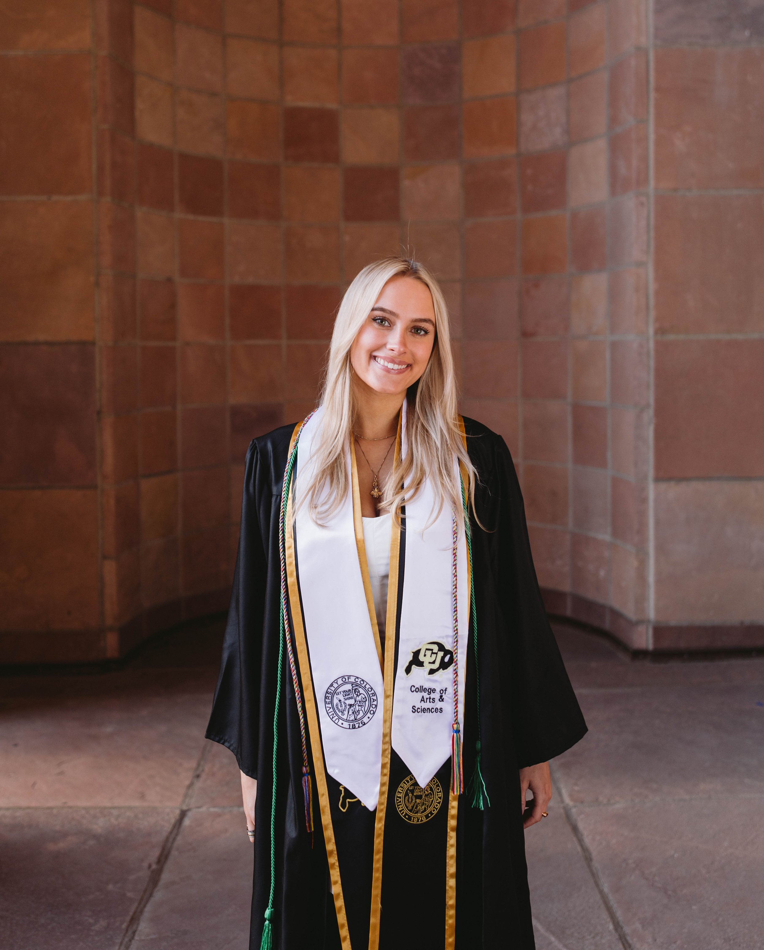 CU Boulder senior portrait in cap and gown under campus archway