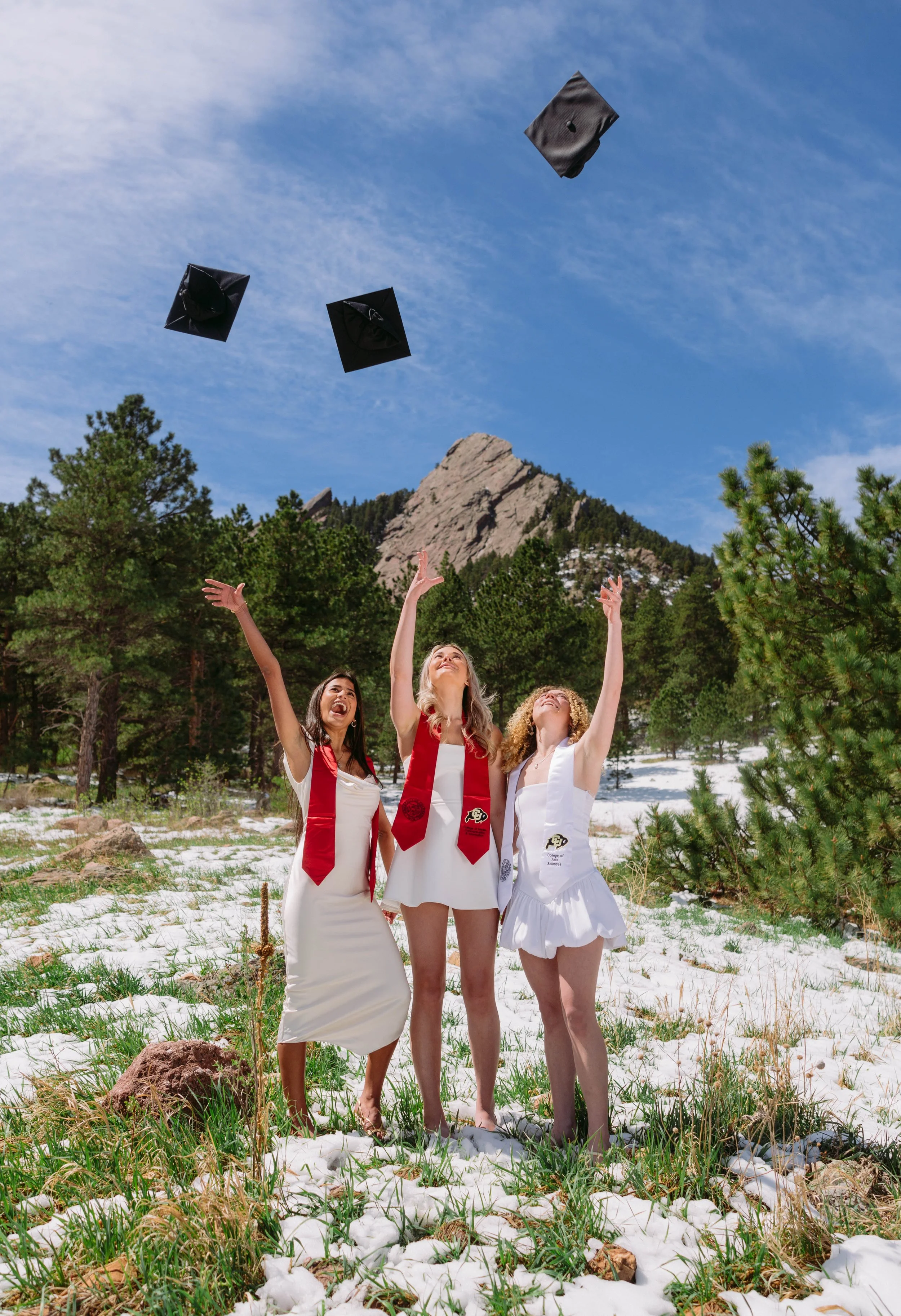 Group of CU Boulder seniors tossing graduation caps with Flatirons mountain backdrop