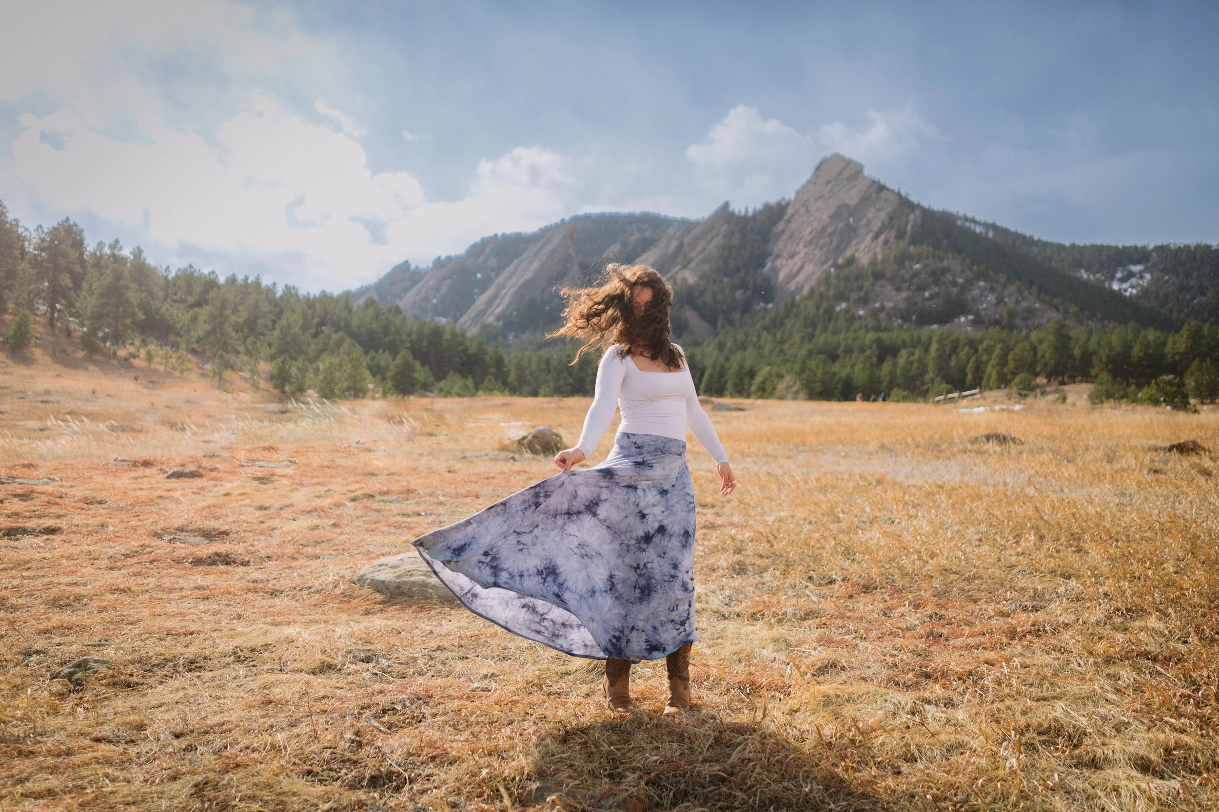 CU Boulder senior twirling dress in open field with Flatirons mountains