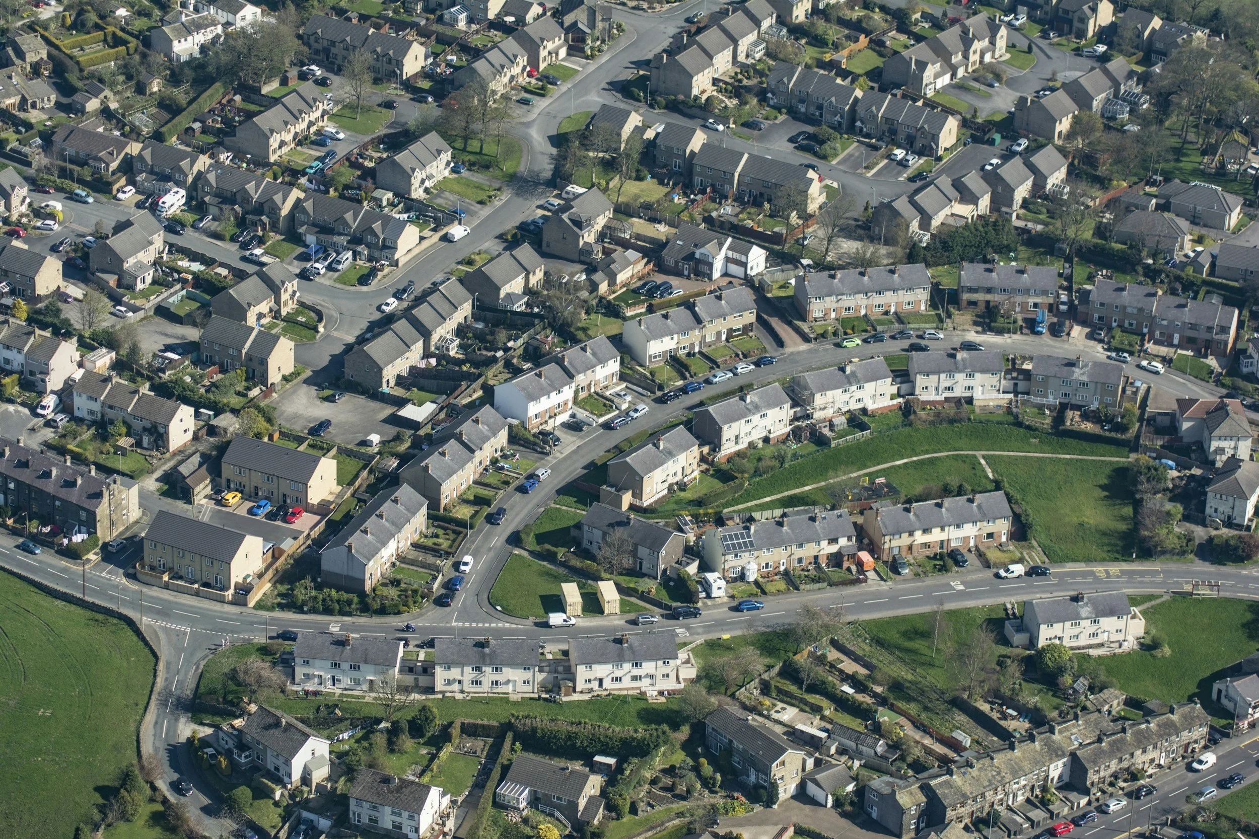 Aerial view of a residential neighborhood with houses, streets, parked cars, and green lawns and trees.