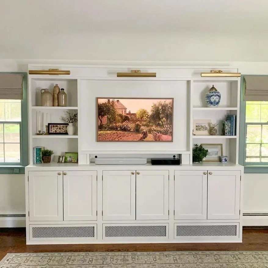 This built in bookcase has inset cabinet doors and removable grates at the base. The grates allow the hydronic baseboard heaters to pump out heat to this cozy room.
