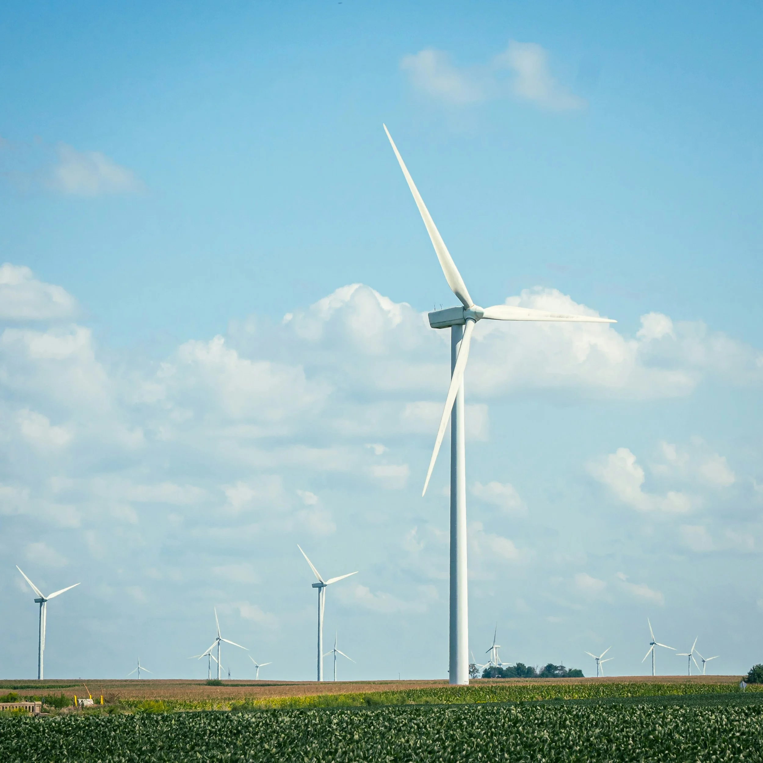 Multiple wind turbines in a field under a partly cloudy sky.