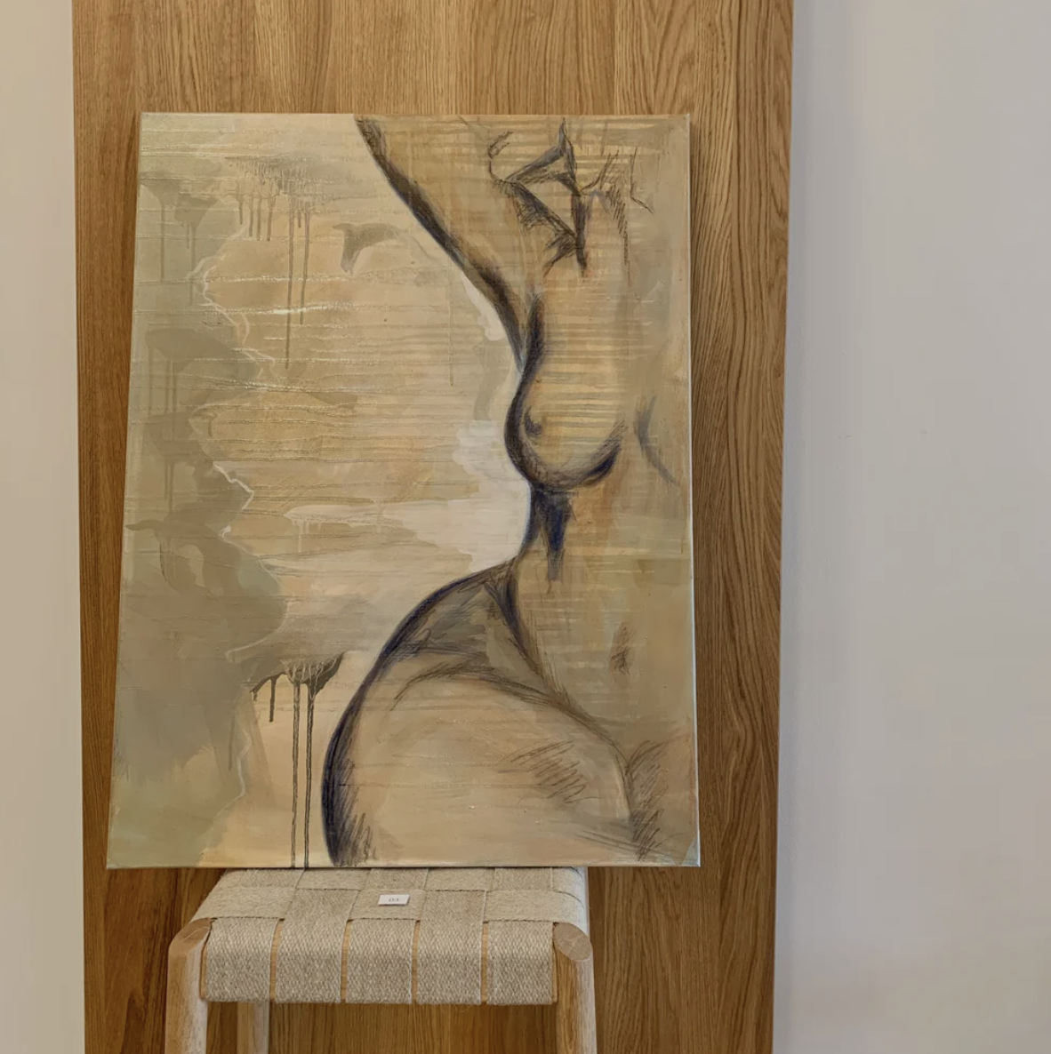 A painting of a woman's profile with soft beige, white, and black tones, emphasizing her facial features and neck, set against a wooden background.