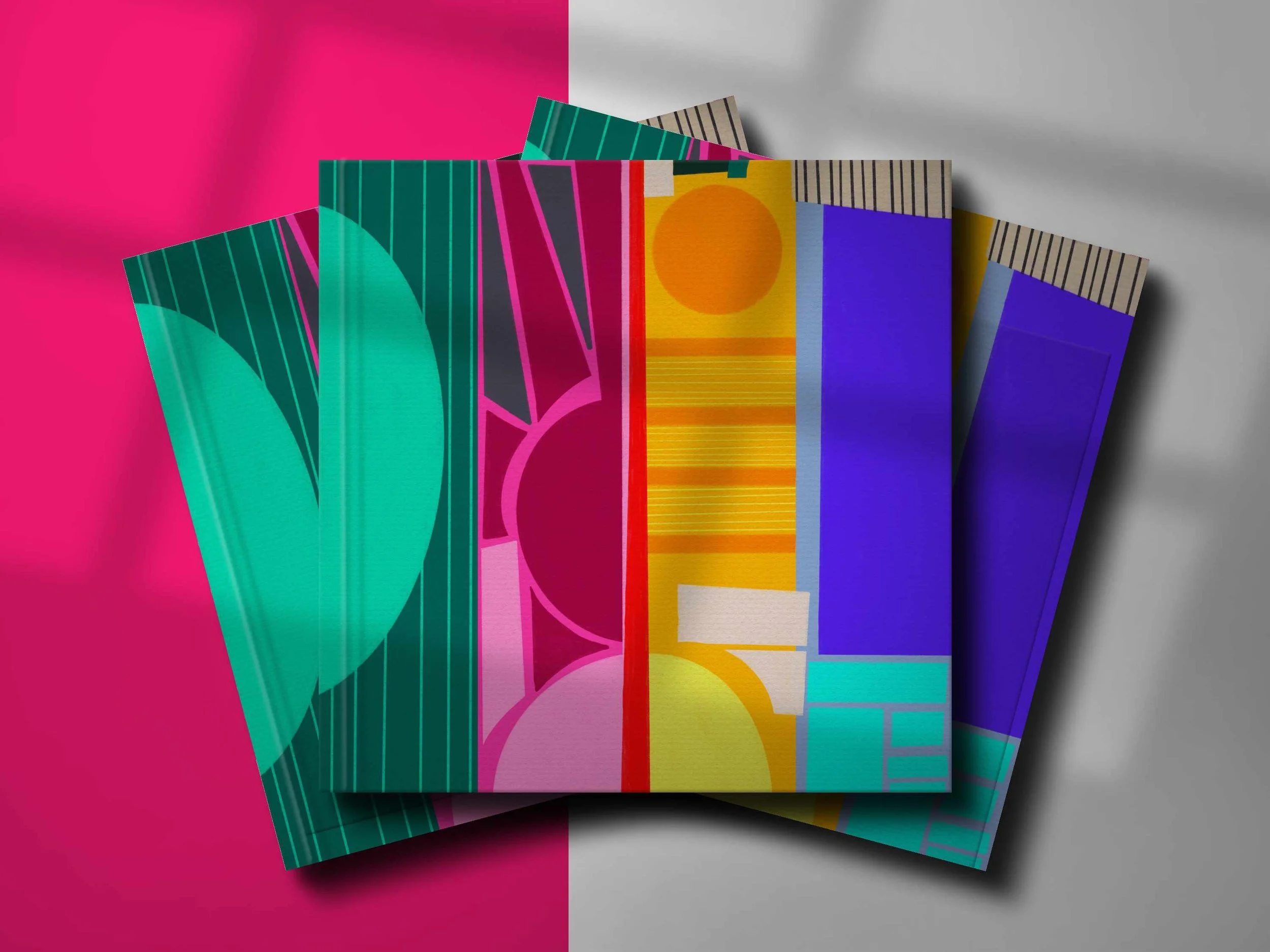 Colorful books or magazines with abstract geometric designs on their covers, placed on a surface divided into pink and gray sections.