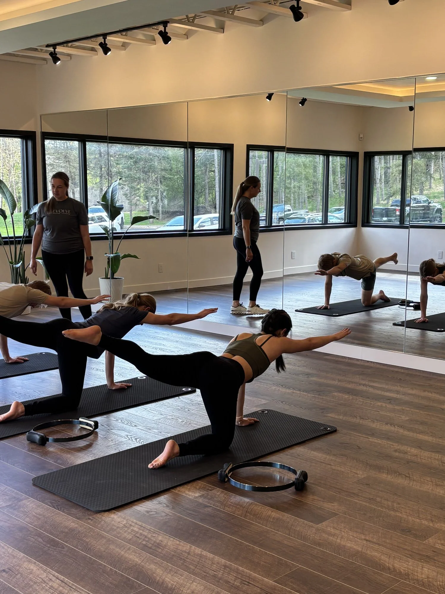 Woman in white sports bra and beige shorts doing a Pilates exercise on a reformer machine in a fitness studio.