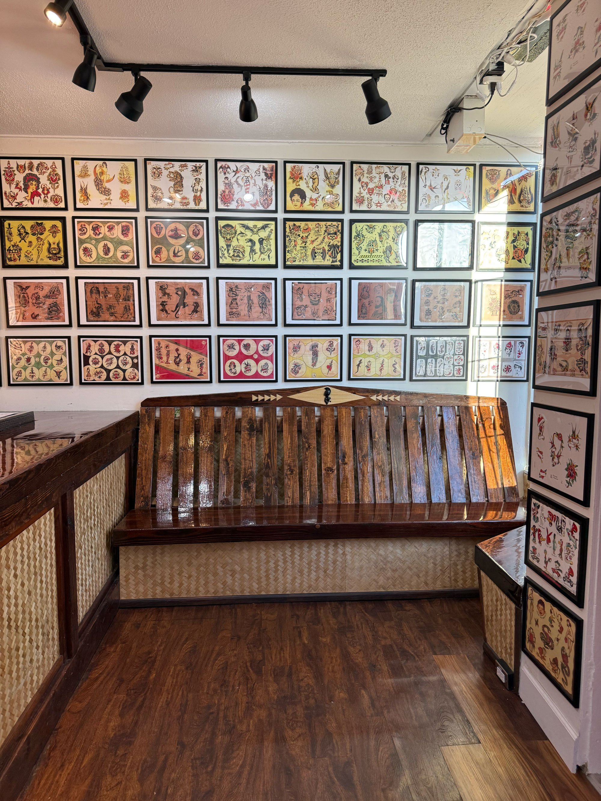Interior of a tattoo shop with tattoo flash art on the walls, a wooden bench, and wooden floors.
