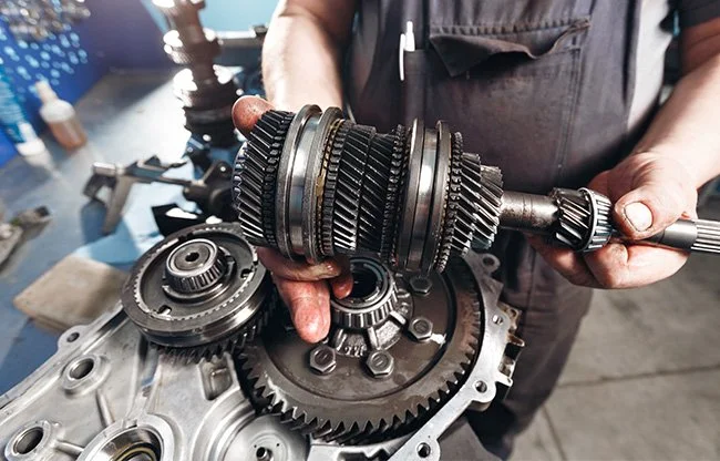 Mechanic holding a gear assembly over a disassembled engine in a workshop.
