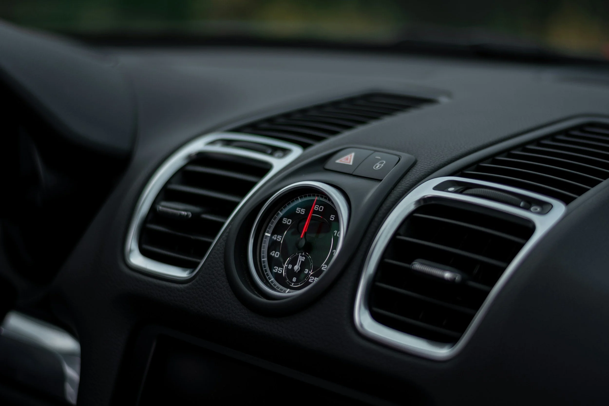 Close-up of a car dashboard featuring an analog clock with a stopwatch function, air vents, and hazard and lock buttons.