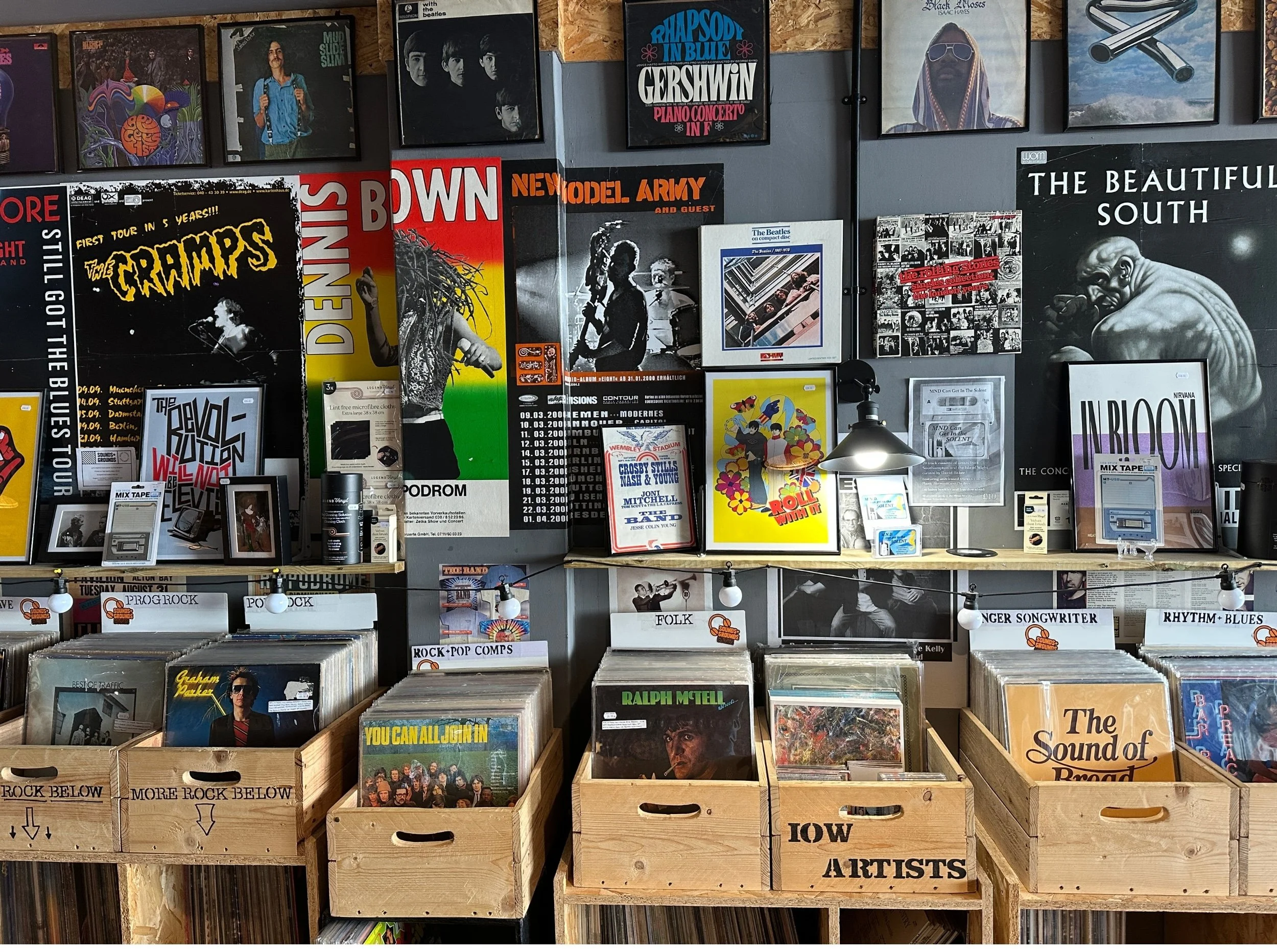 Wooden Crates of Vinyl Albums are stacked in front of a grey wall covered in album posters at Sounds and Grounds Isle of Wight Record Shop