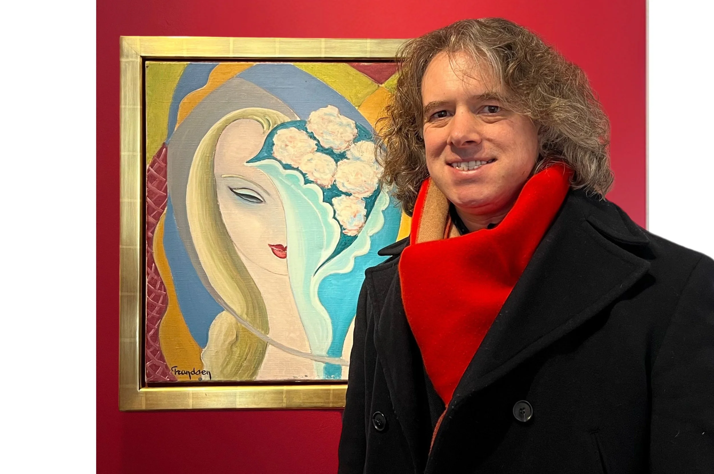 A handsome man with a red scarf and back coat stands next to the original artwork for the Layla album