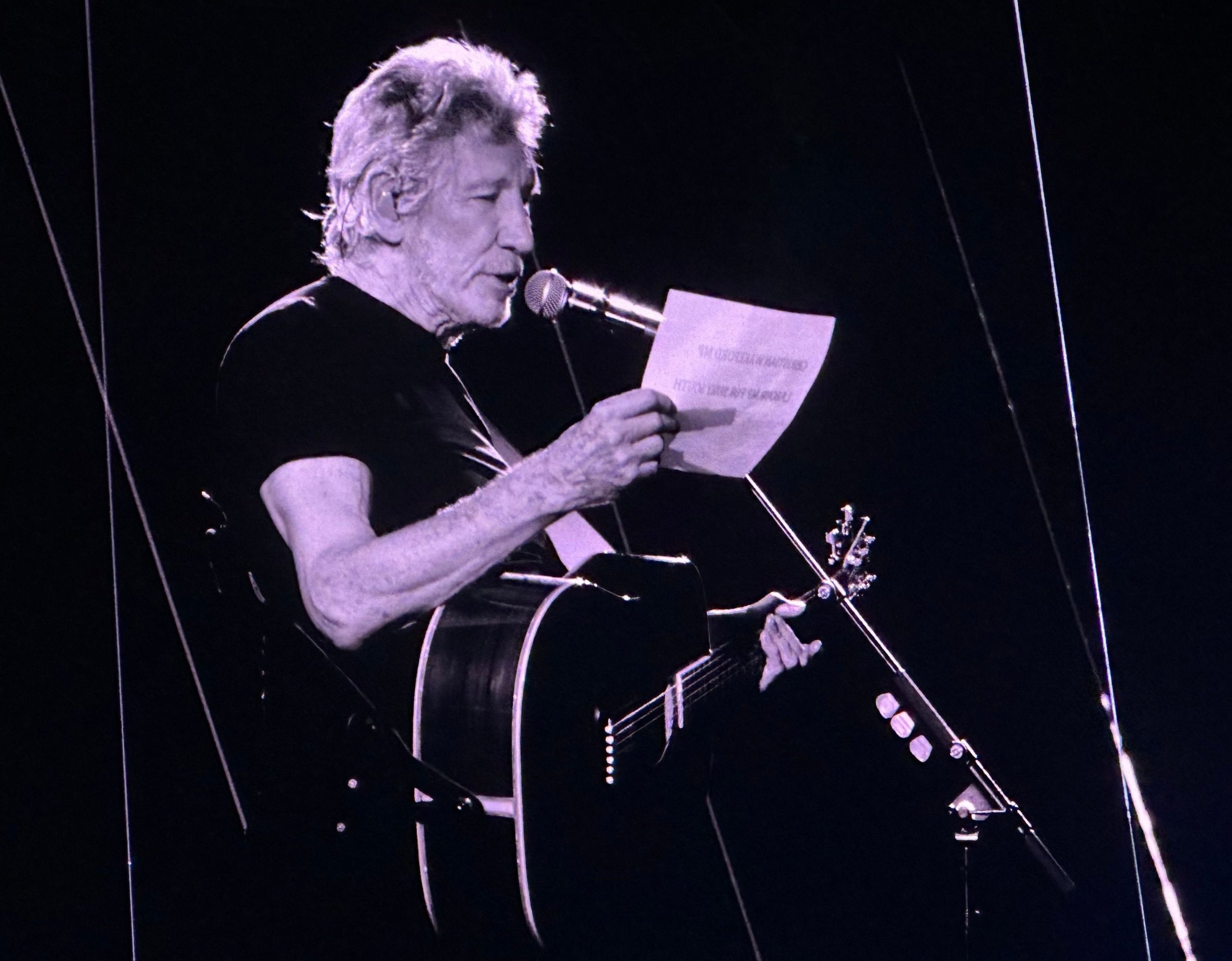 Roger Waters reading a handwritten letter to the Birmingham crowd with an acoustic guitar slung over his shoulder during This Is Not A Drill.