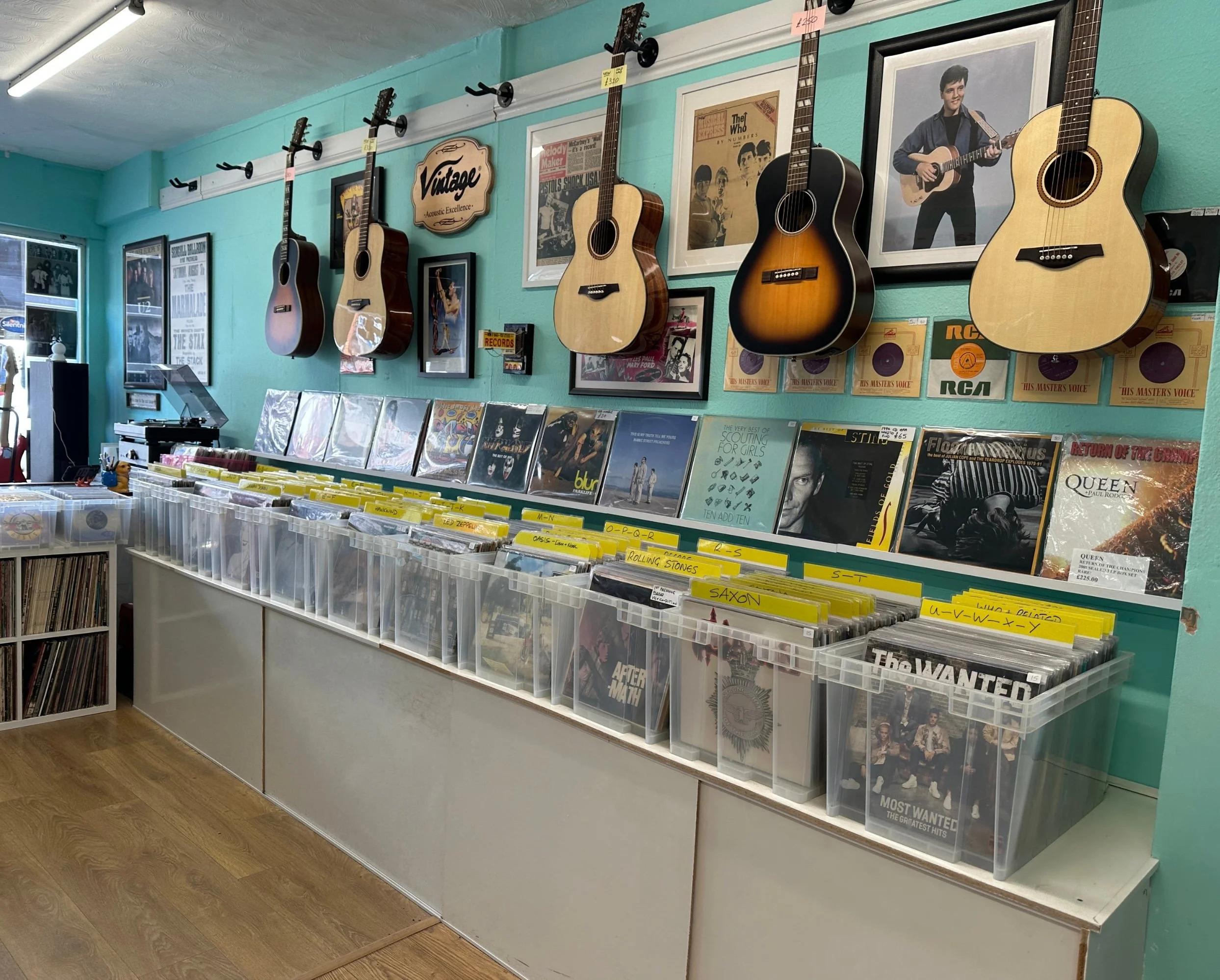 A pale blue wall is adorned with guitars, framed pictures and vinyl album covers