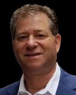 Close-up of a smiling man in a blue suit and white shirt on a black background.