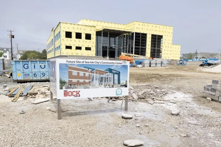 Construction site with a building under development, a sign showing a digital rendering of the future Sea Isle City Community Center, and construction materials scattered around.