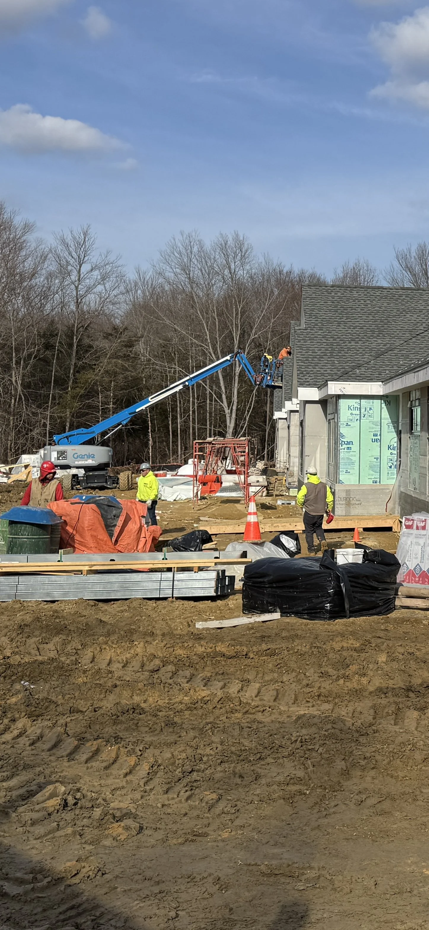 Construction workers and equipment working on a building site under a blue sky.