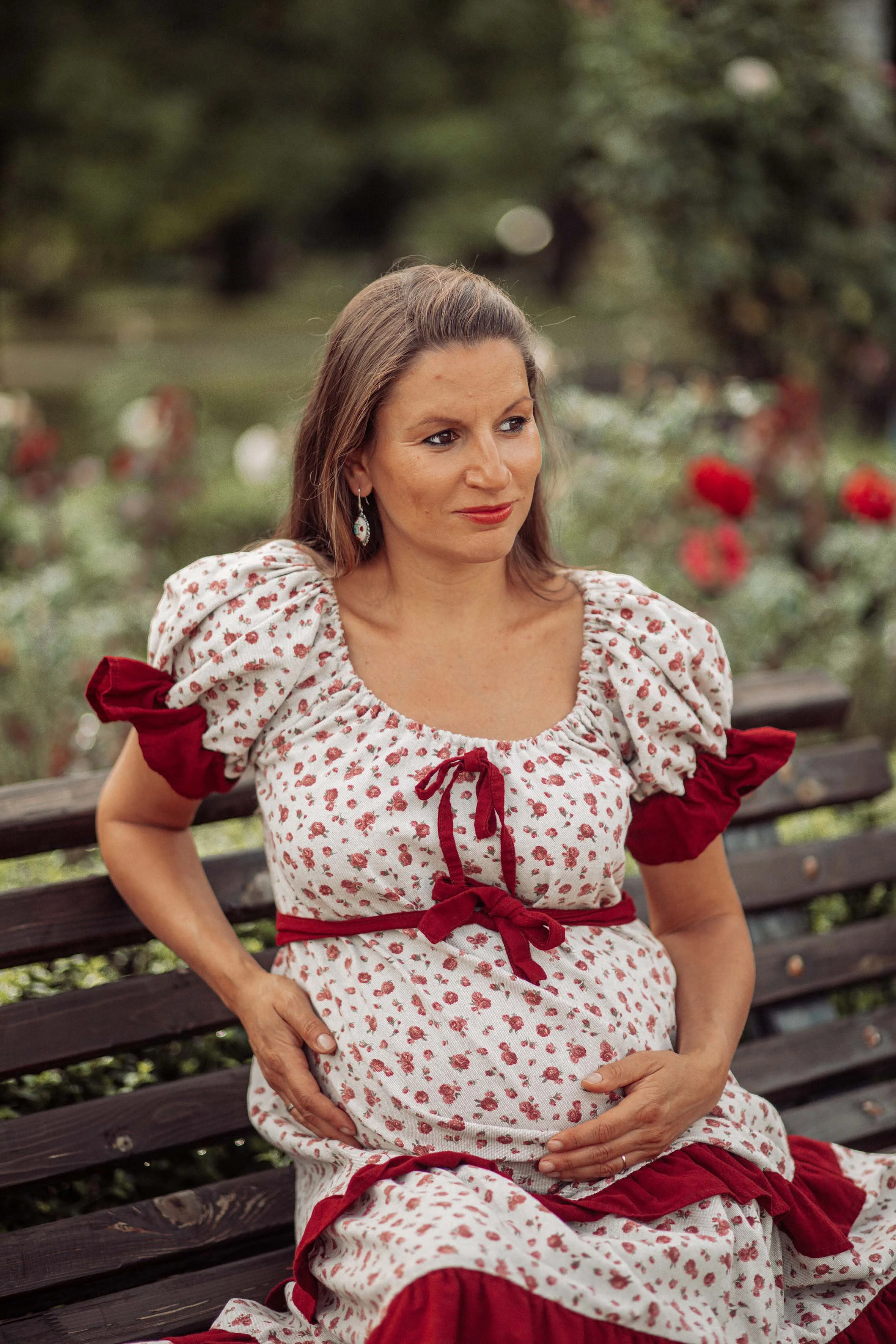 beautiful pregnant woman dressed a boho dress in a garden of red roses