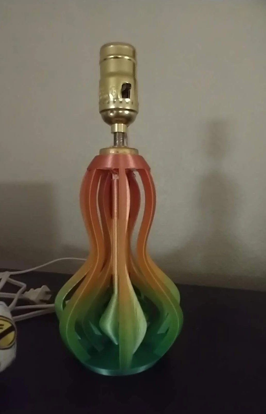 Colorful table lamp with a rainbow gradient, no shade, on a dark surface next to a power cord.