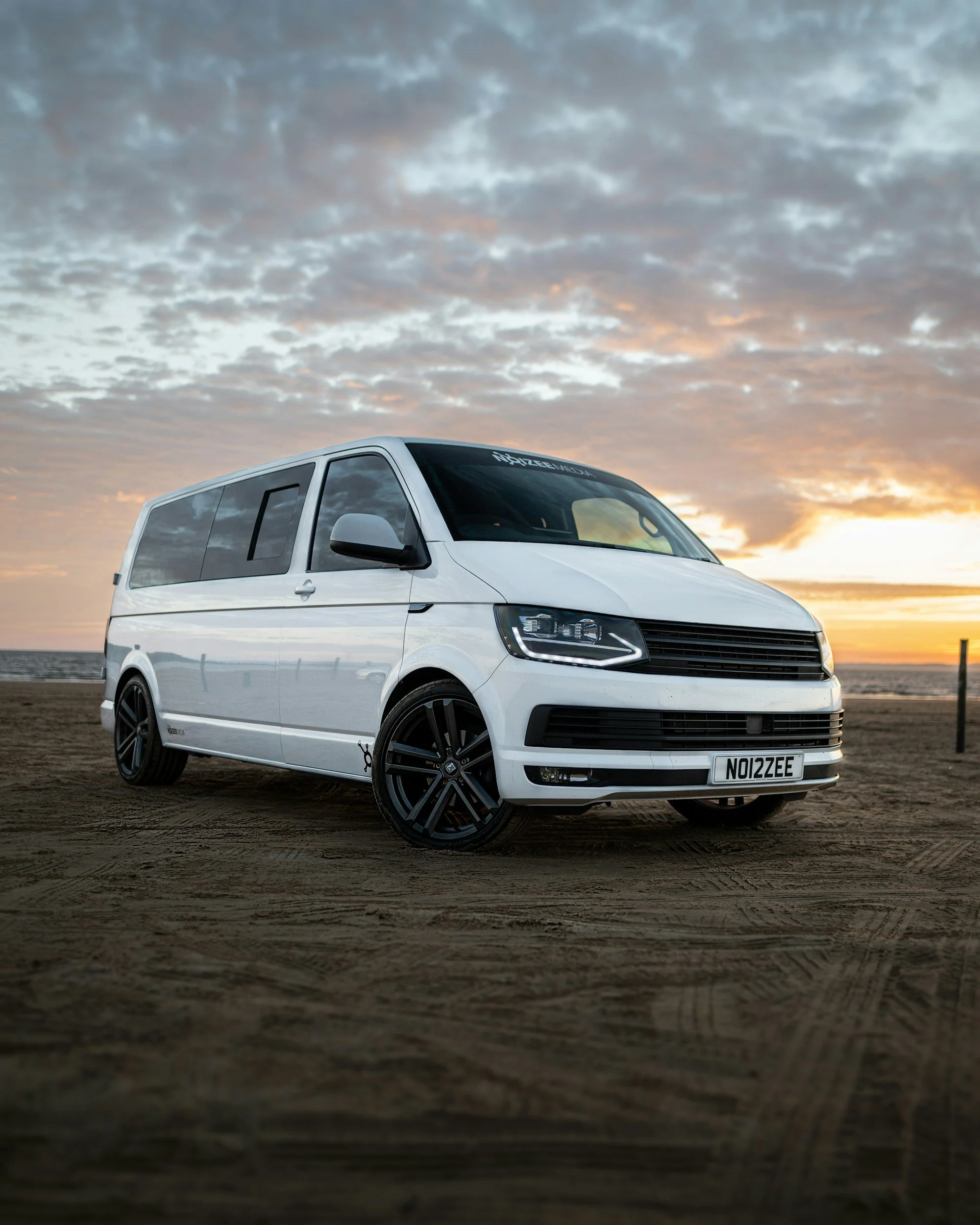White van parked on sandy beach during sunset, with a cloudy sky in the background.